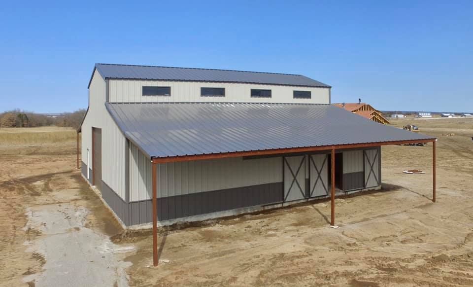An aerial view of a barn with a covered porch in a field.