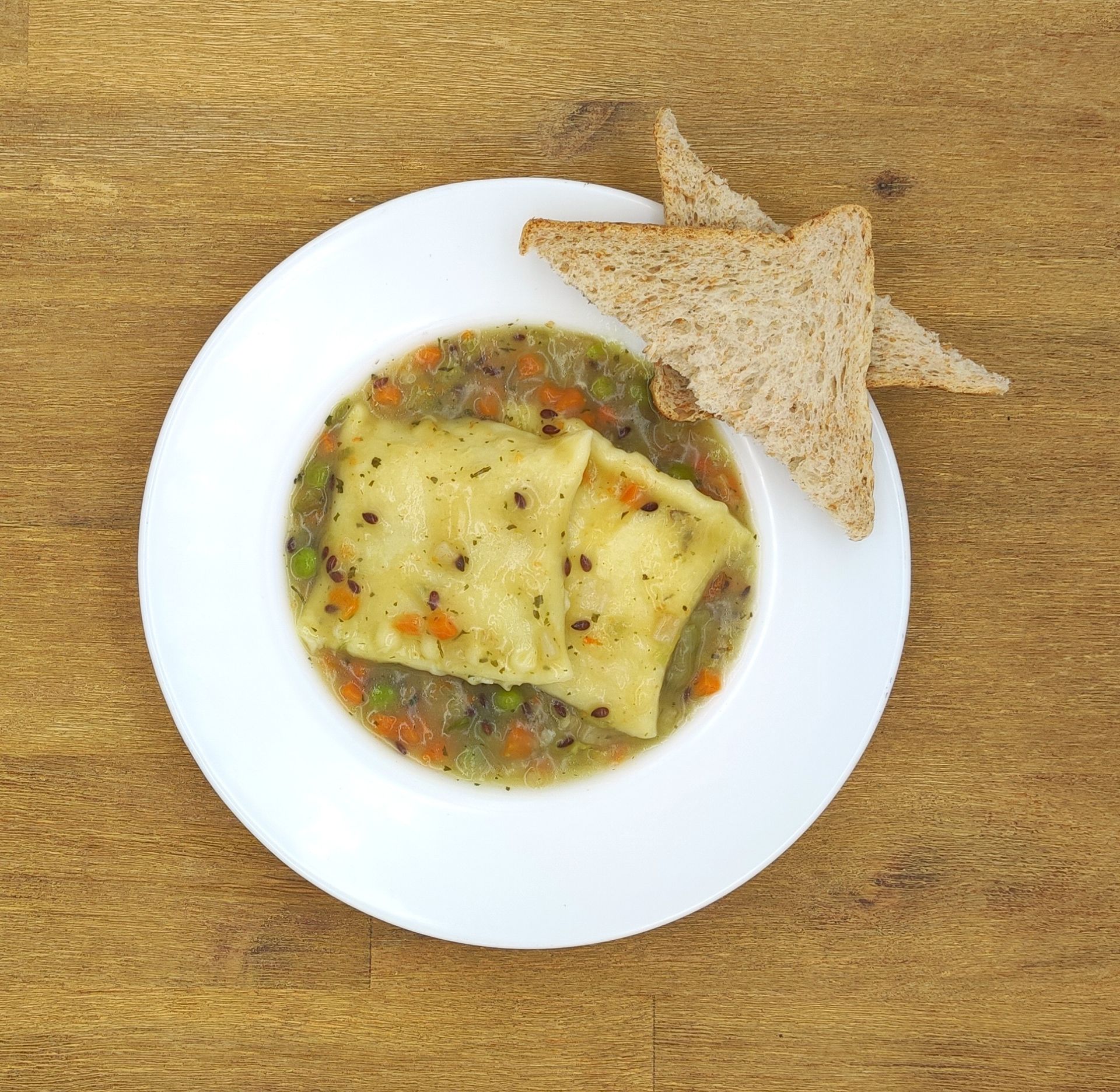 Ein Teller Ravioli in Brühe mit Toast auf einem Holztisch.