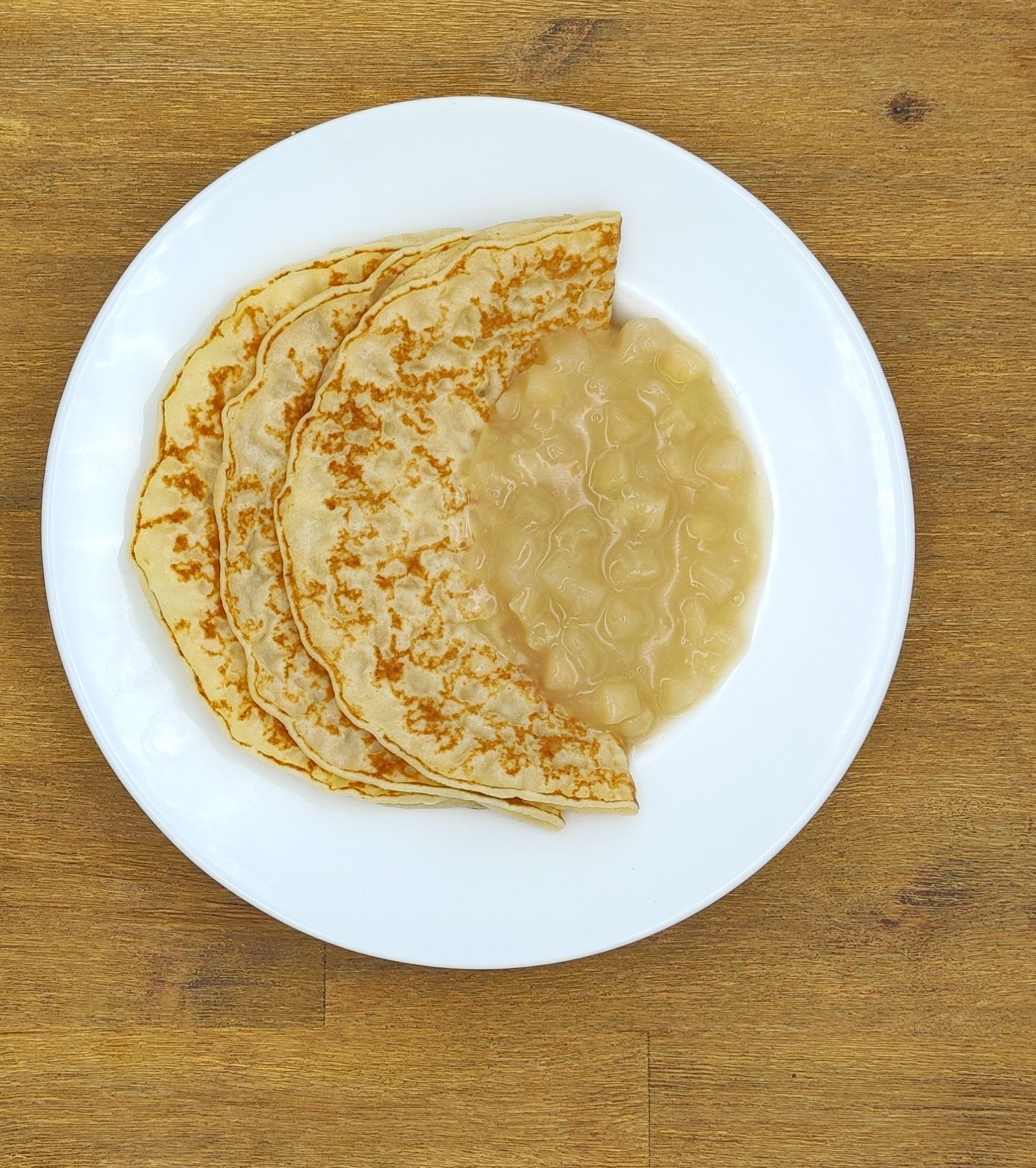 Crêpes mit Apfelmus auf einem weißen Teller, der auf einer Holzoberfläche steht.