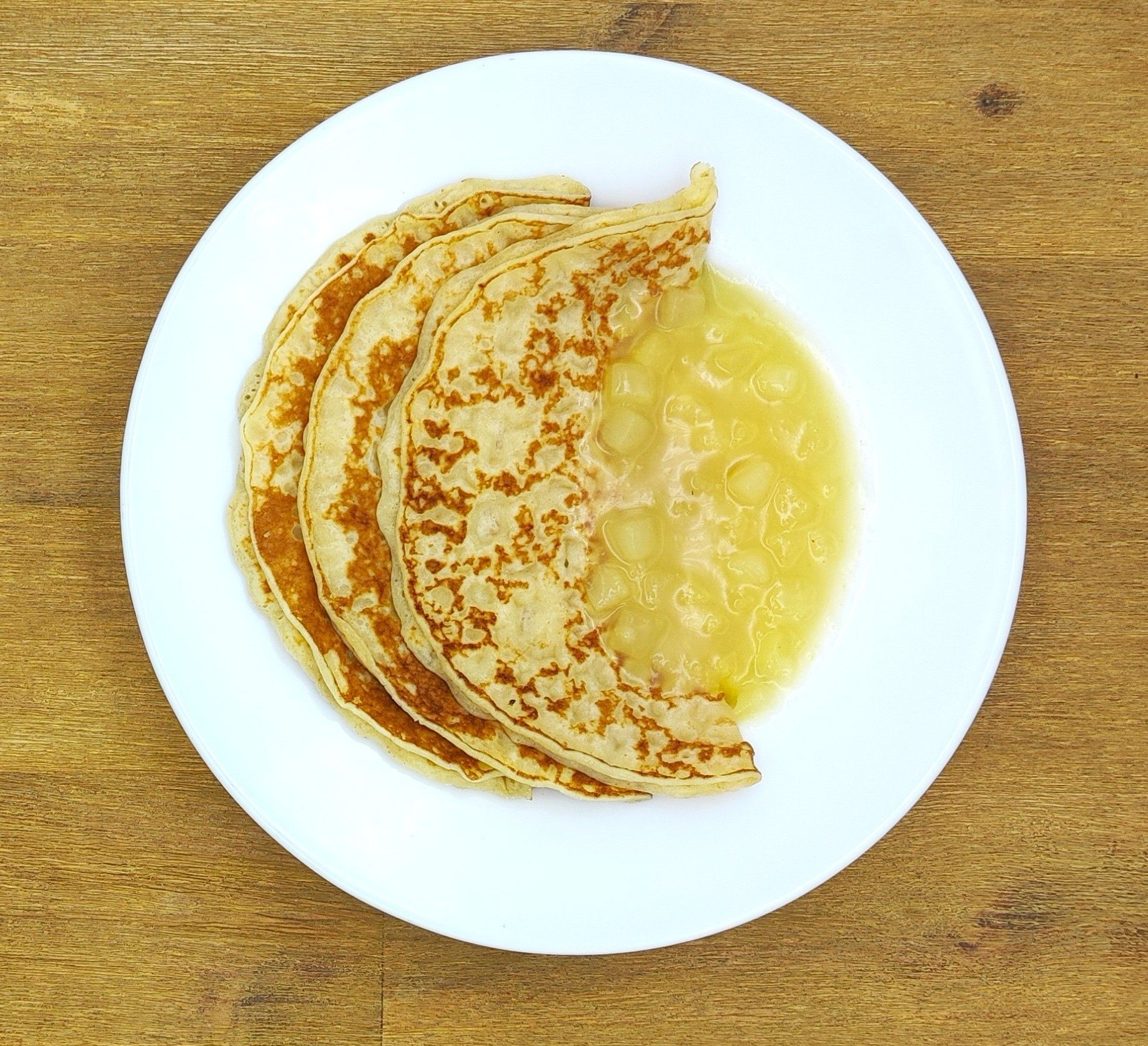 Drei Crêpes auf einem weißen Teller mit Apfelmus, auf einer Holzoberfläche.
