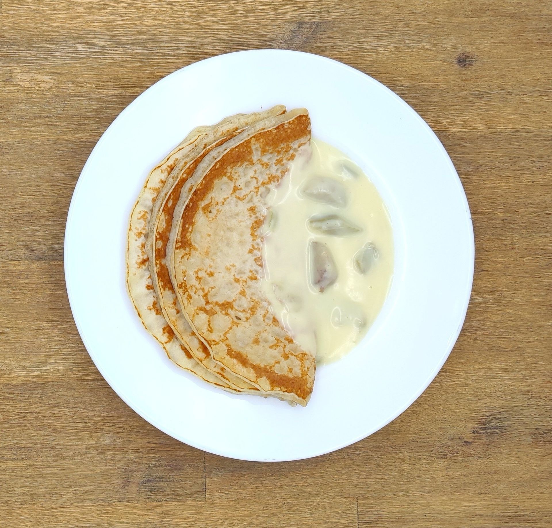 Auf einem weißen Teller mit Apfelmus lagen Crêpes auf einem Holztisch.