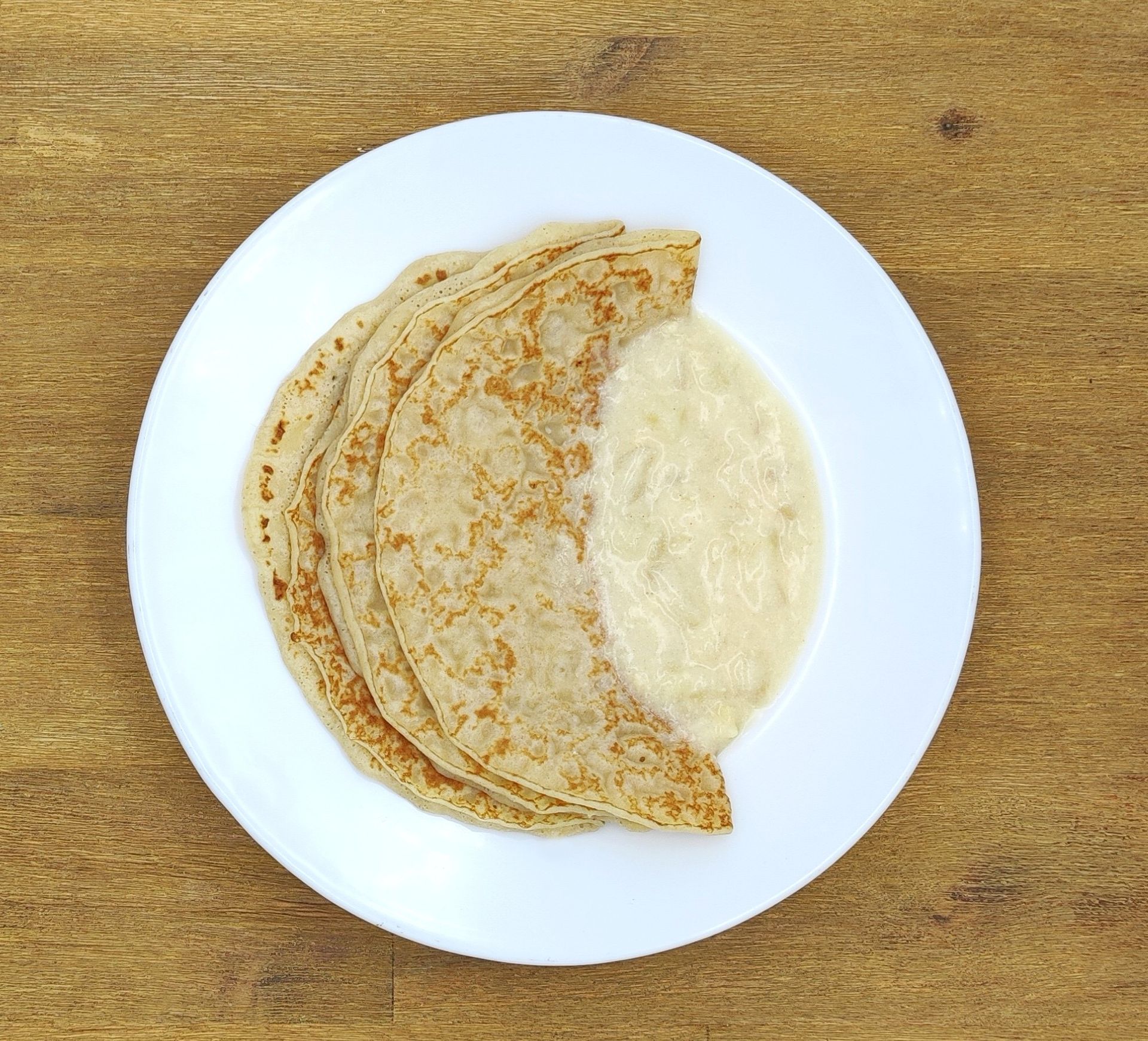 Pfannkuchen auf einem weißen Teller mit Soße, auf einer Holzoberfläche.