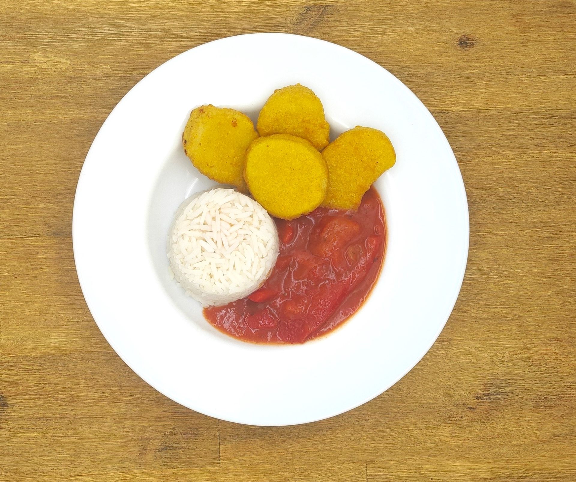 Teller mit frittiertem Essen, weißem Reis und Tomatensoße auf einer Holzoberfläche.