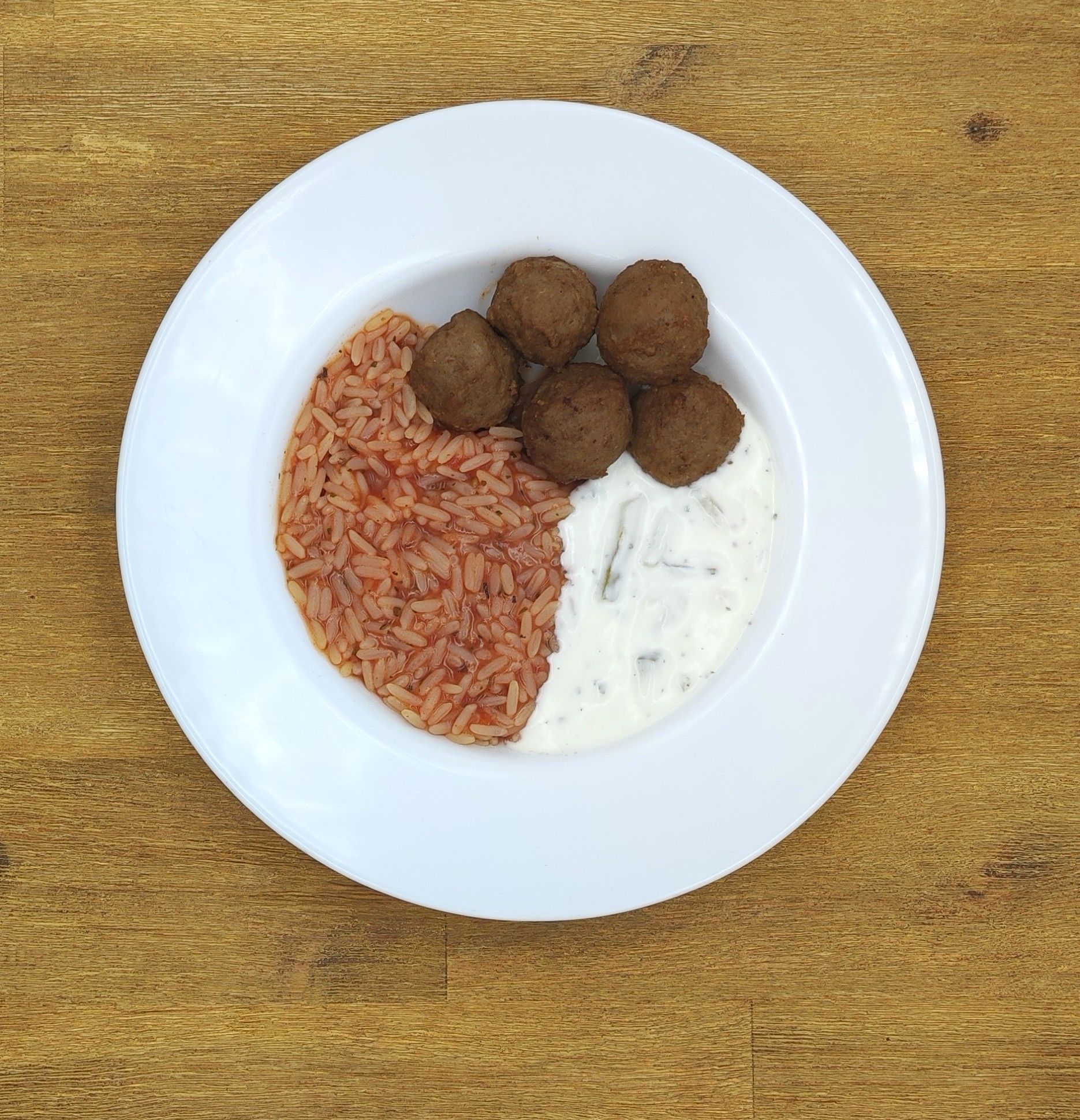 Ein Teller mit Falafel, Reis und weißer Soße auf einem Holztisch.