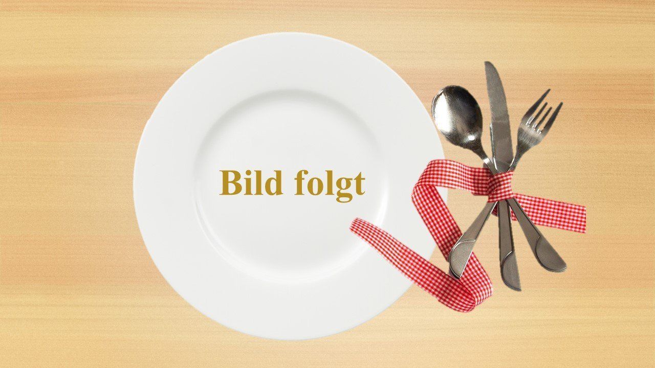 Weißer Teller mit der Aufschrift „Bild folgt“, Besteck, mit rotem Band zusammengebunden, auf einem Holztisch.