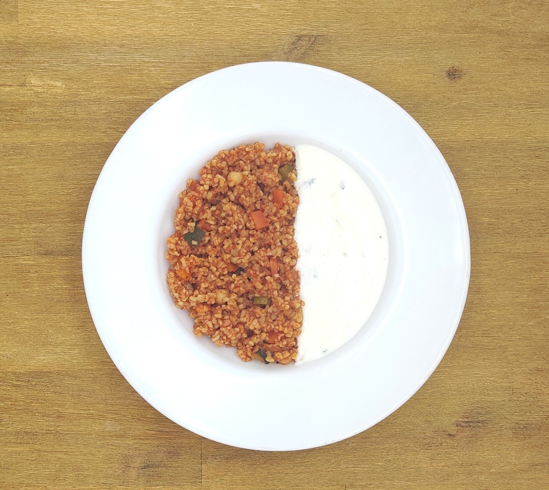 Teller mit Speisen: halb herzhafte Getreidemischung, halb weiße Sahnesauce.