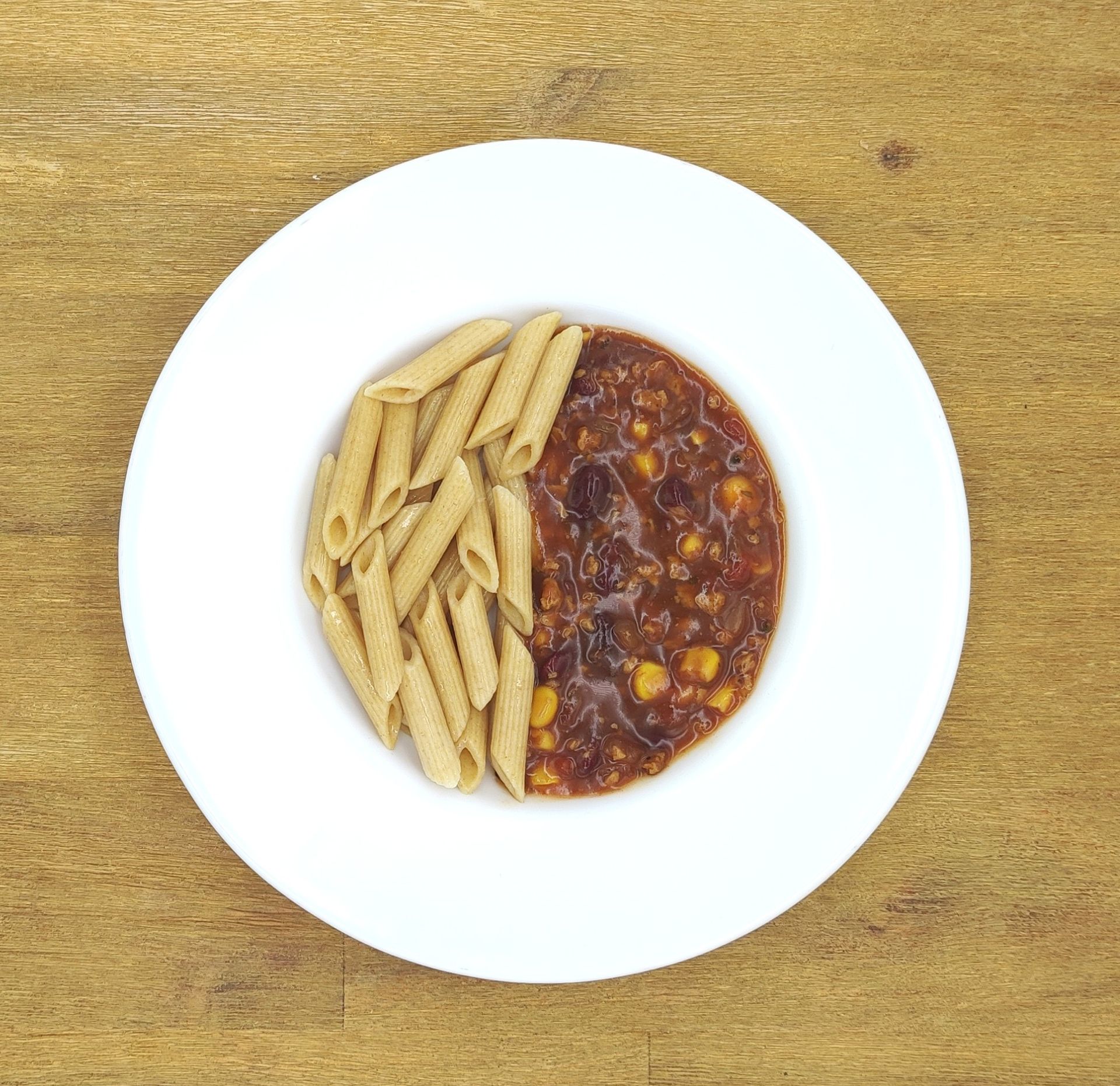 Weiße Schüssel mit Linsensuppe und Brot auf einer Holzoberfläche.