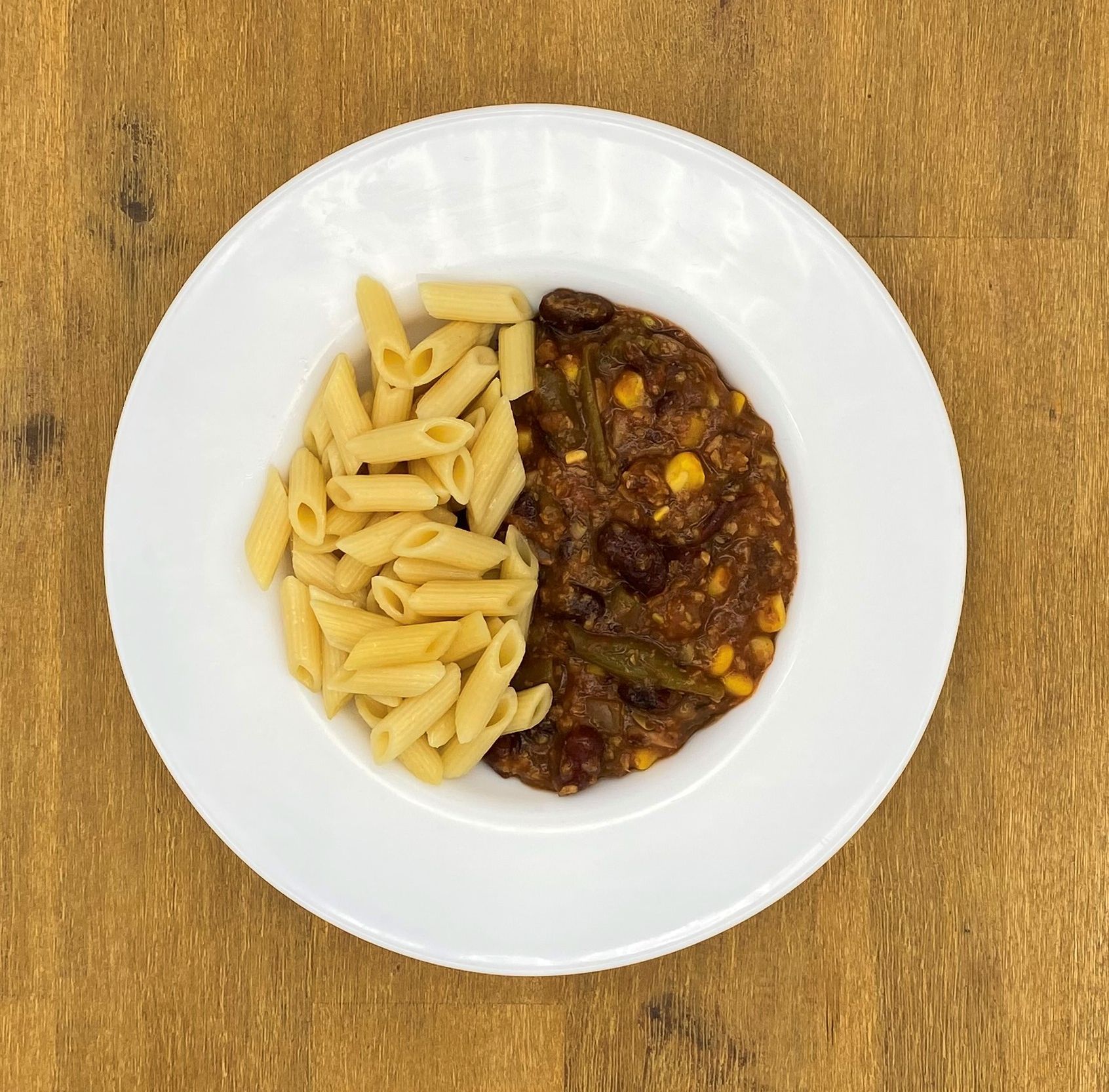 Weiße Schüssel mit Linsensuppe und Brot auf einer Holzoberfläche.