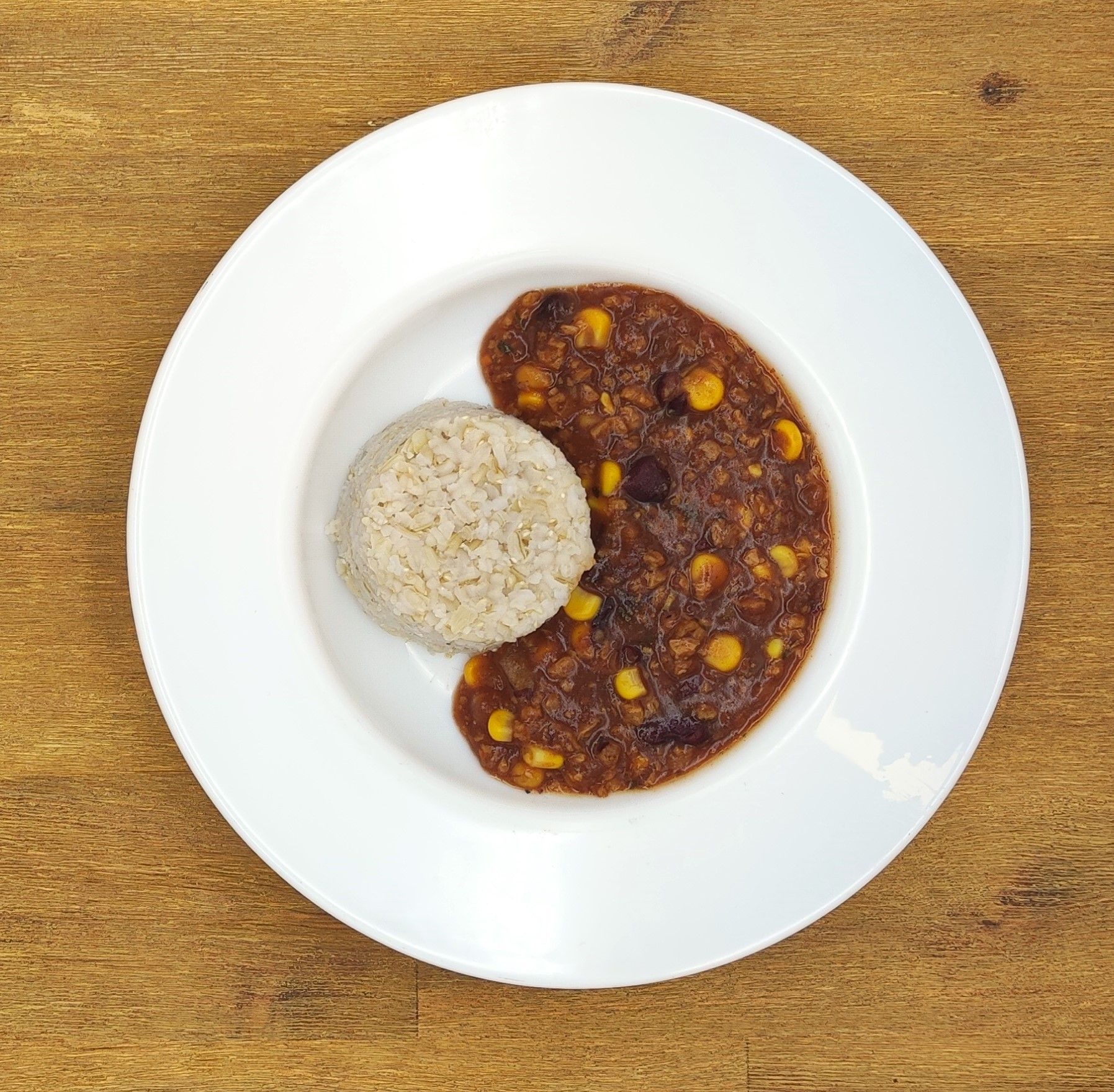 Weißer Teller mit einer Kugel Reis und Chili mit Mais.