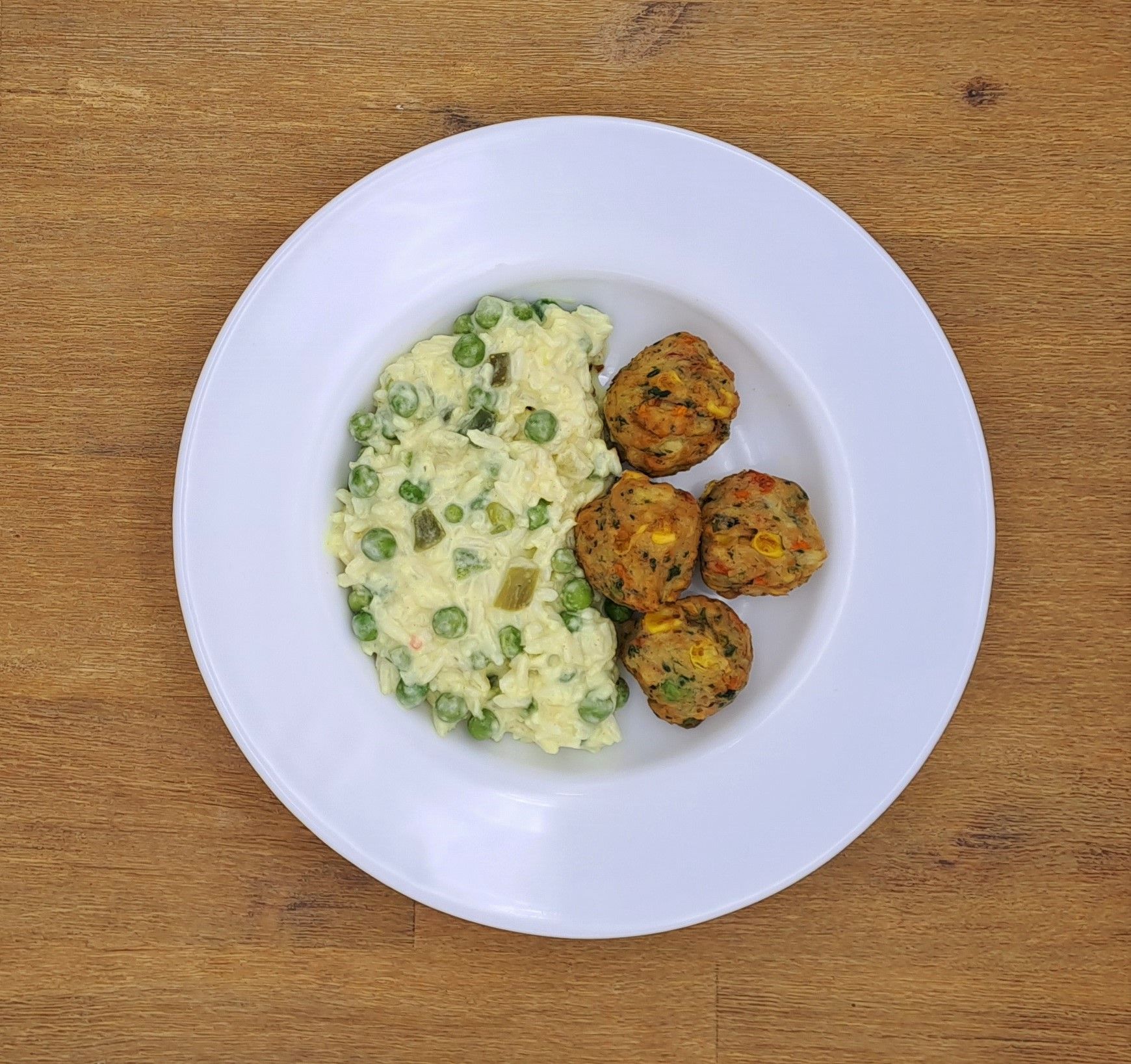Weißer Teller mit Risotto und drei Fleischbällchen auf einer Holzoberfläche.