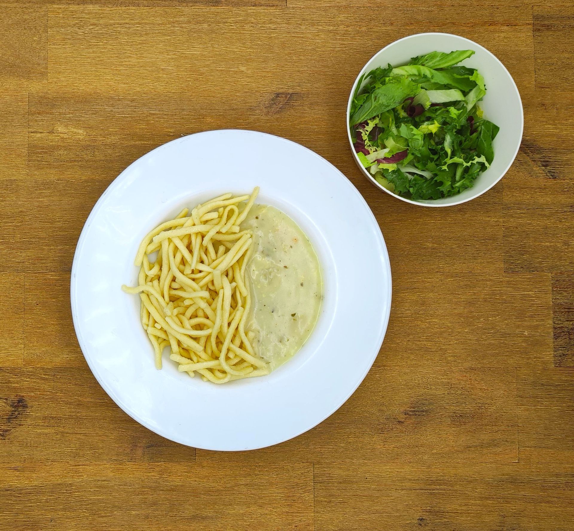 Pastagericht mit Sahnesauce und Beilagensalat auf einem Holztisch.