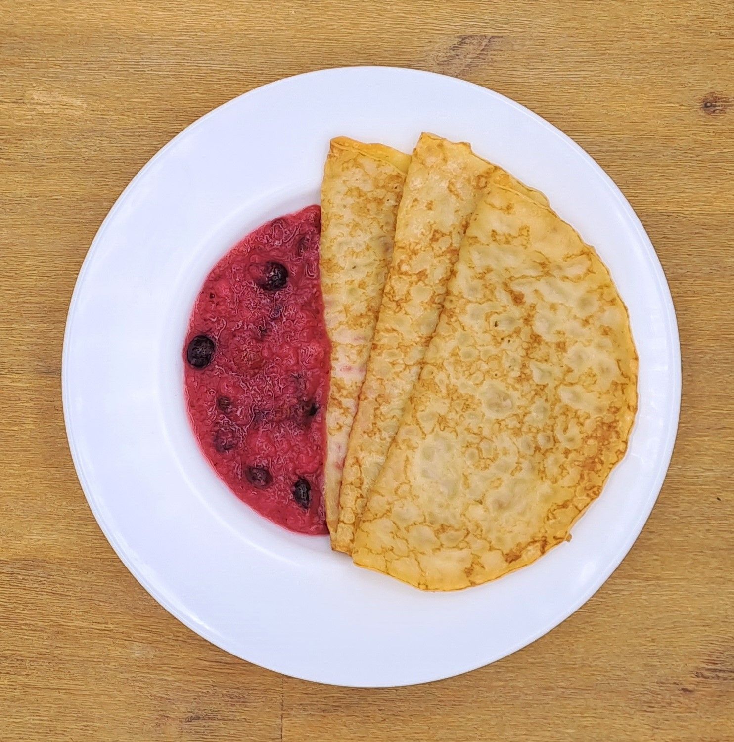 Teller mit Crêpes und einer rosa Beerensauce.