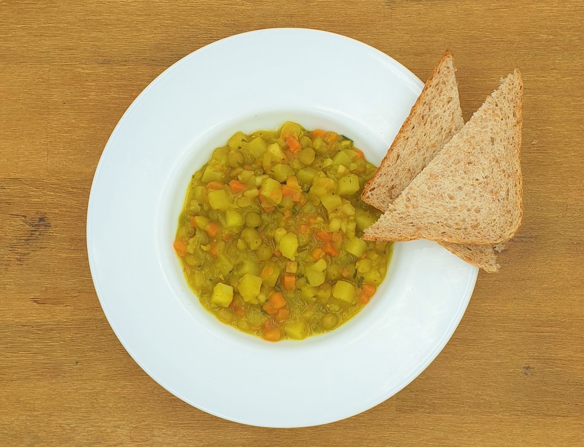 Weiße Schüssel mit Eintopf und zwei Toastdreiecke auf einem Holztisch.