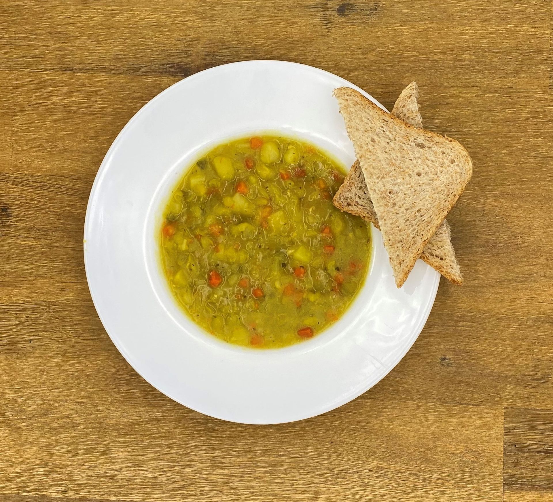 Suppe in einer weißen Schüssel mit geröstetem Brot auf einem Holztisch.