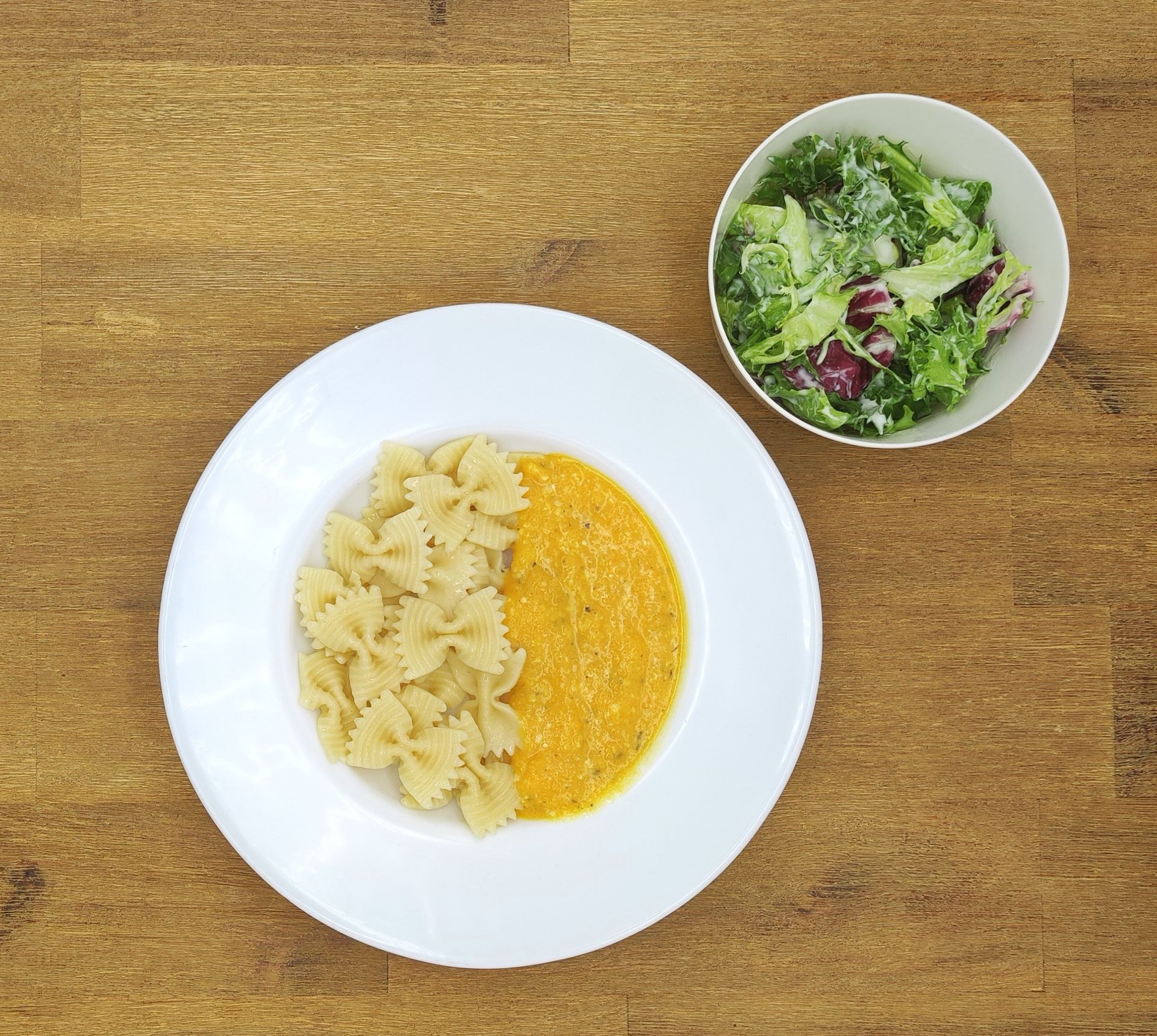 Pasta mit Orangensauce und einem Beilagensalat in einer Schüssel auf einem Holztisch.