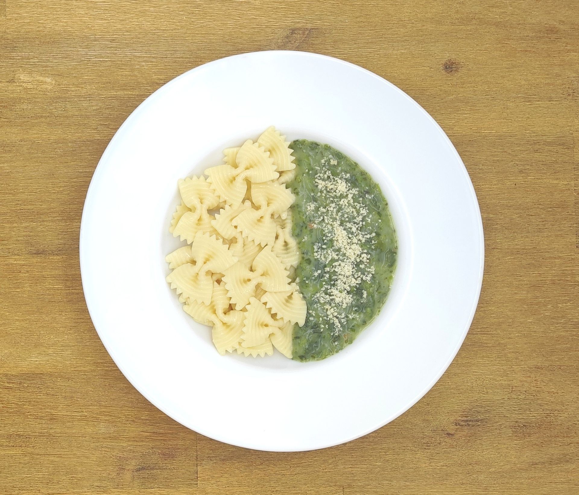 Pasta mit grüner Soße und Parmesan auf einem weißen Teller, Holztisch.