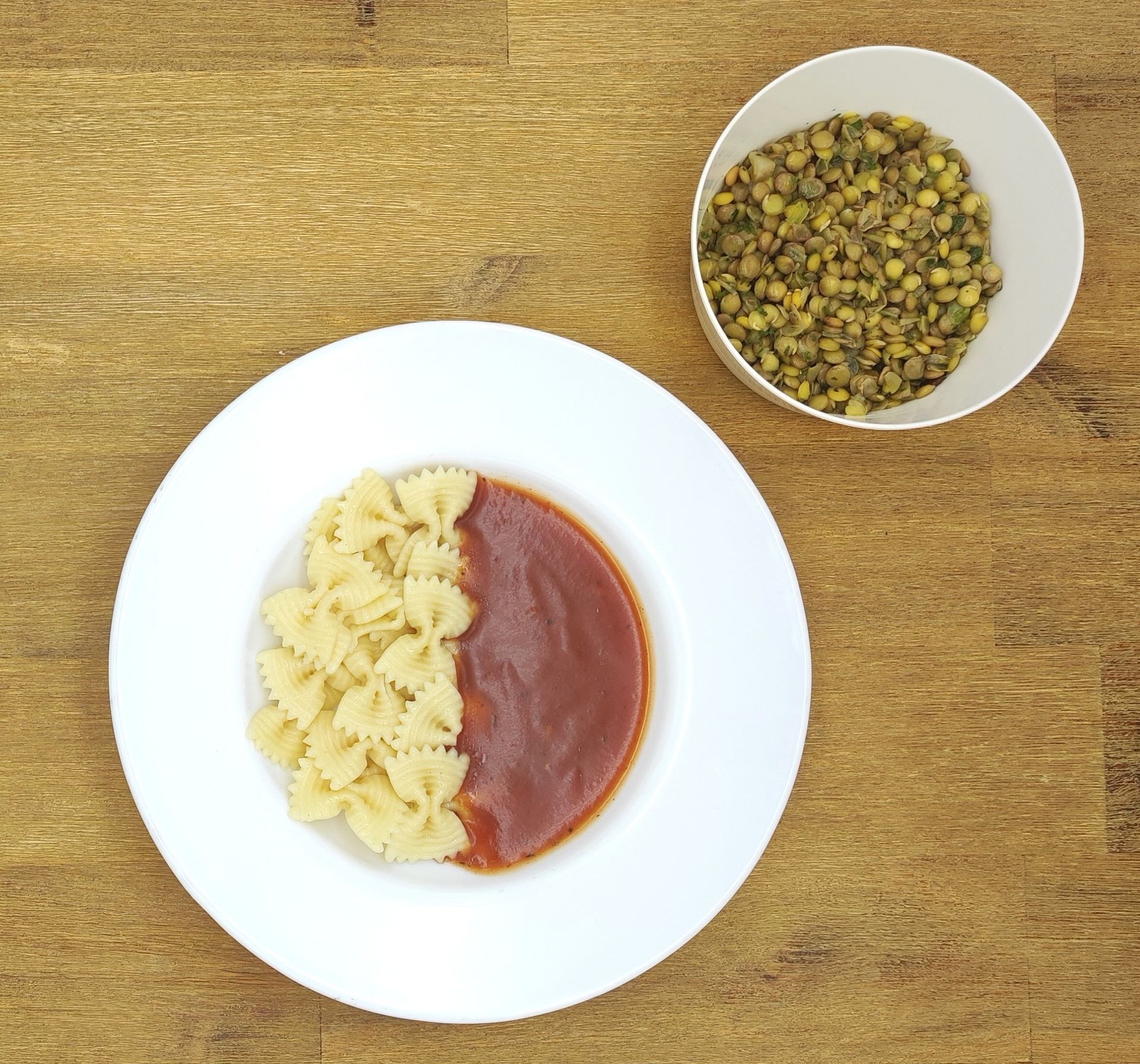 Weißer Teller mit Farfalle-Nudeln und Orangensauce, bestreut mit geriebenem Käse.