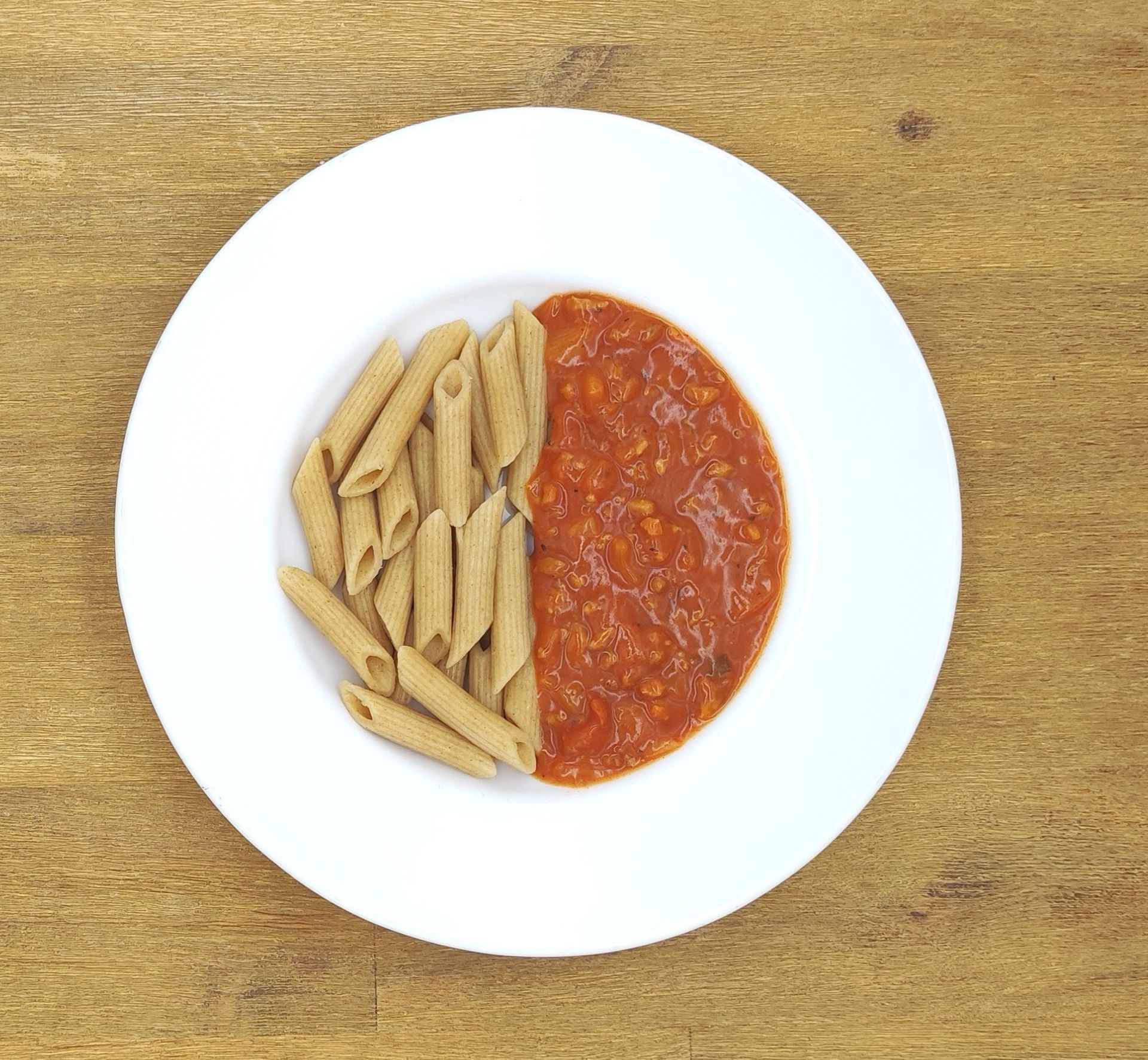 Pasta mit Tomatensoße auf einem weißen Teller, der auf einer Oberfläche mit Holzmaserung steht.
