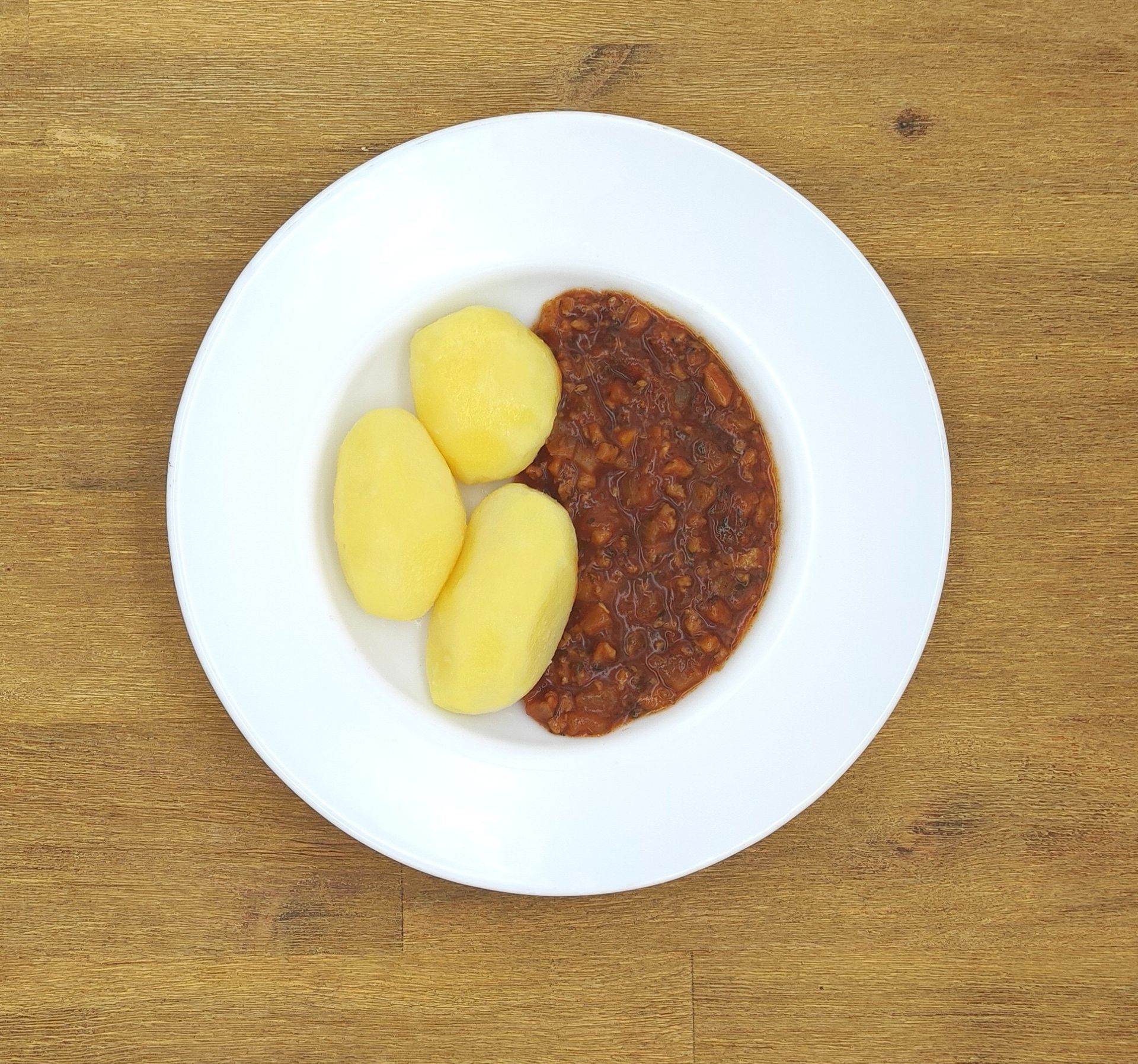Weißer Teller mit drei gelben Kartoffeln und einem Klecks brauner Soße.