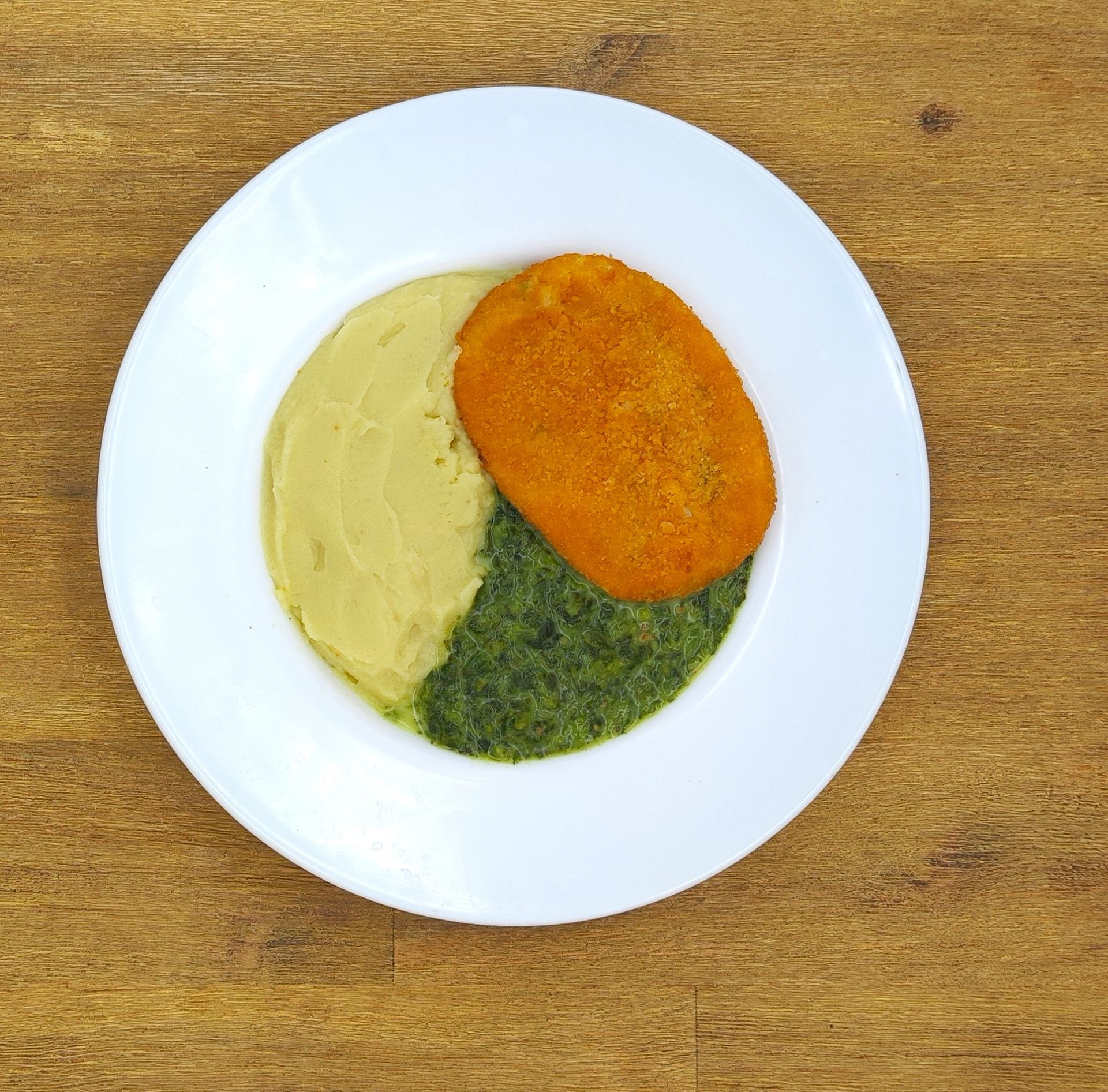 Ein weißer Teller mit einem panierten Schnitzel auf Kartoffelpüree und Spinat.