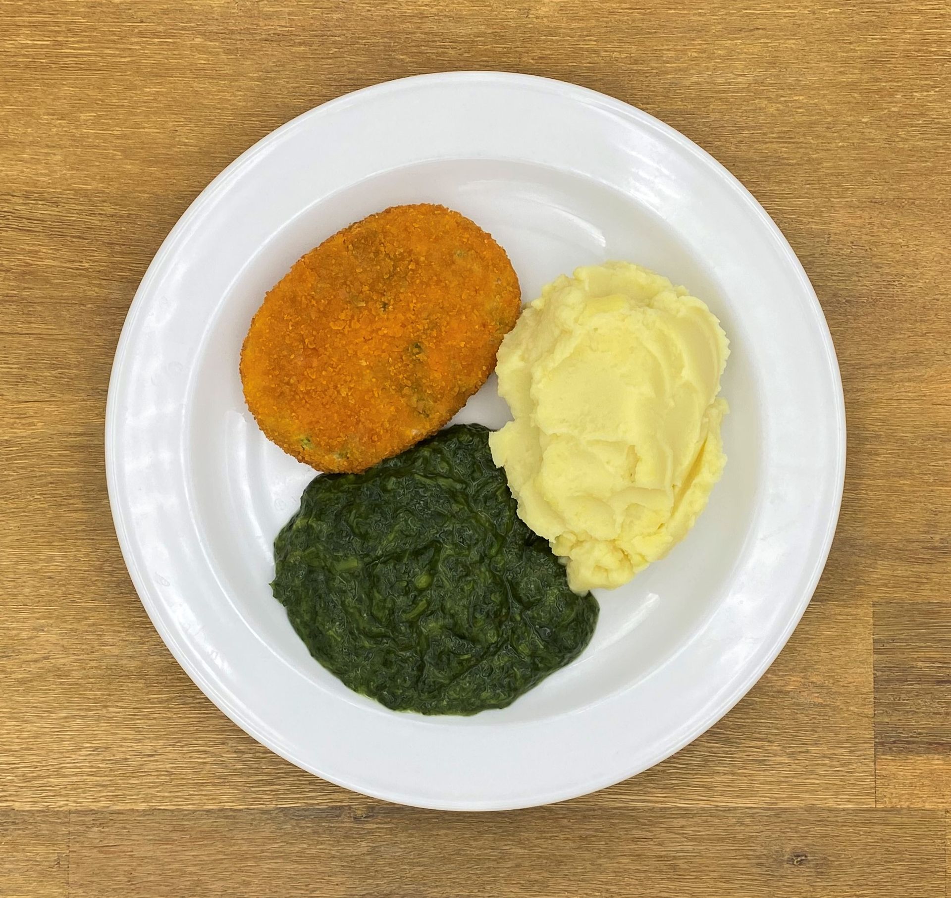 Teller mit Essen: paniertes Frikadelle, Kartoffelpüree und Spinat.