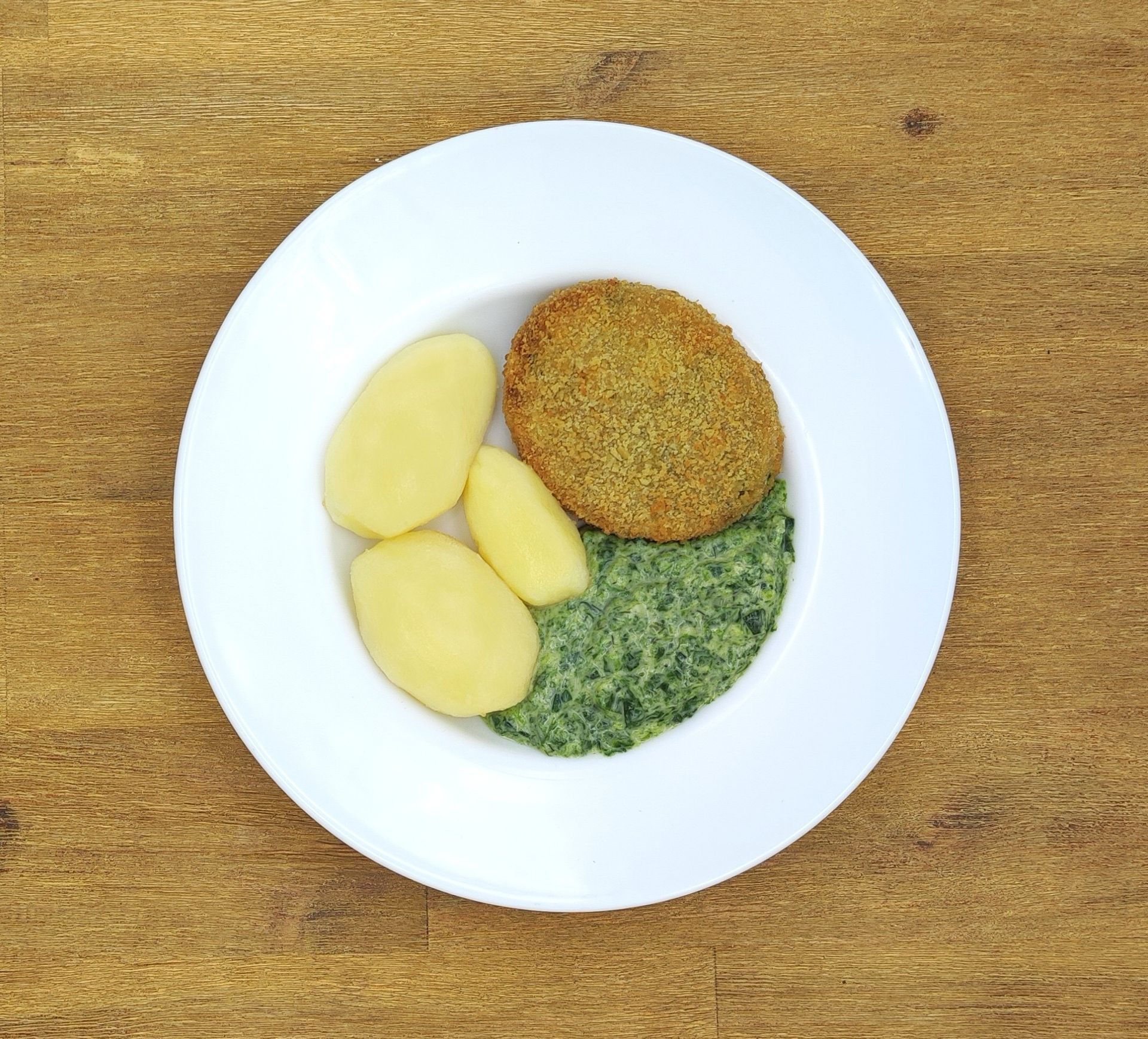 Teller mit Essen: paniertes Frikadelle, Rahmspinat und Salzkartoffeln.