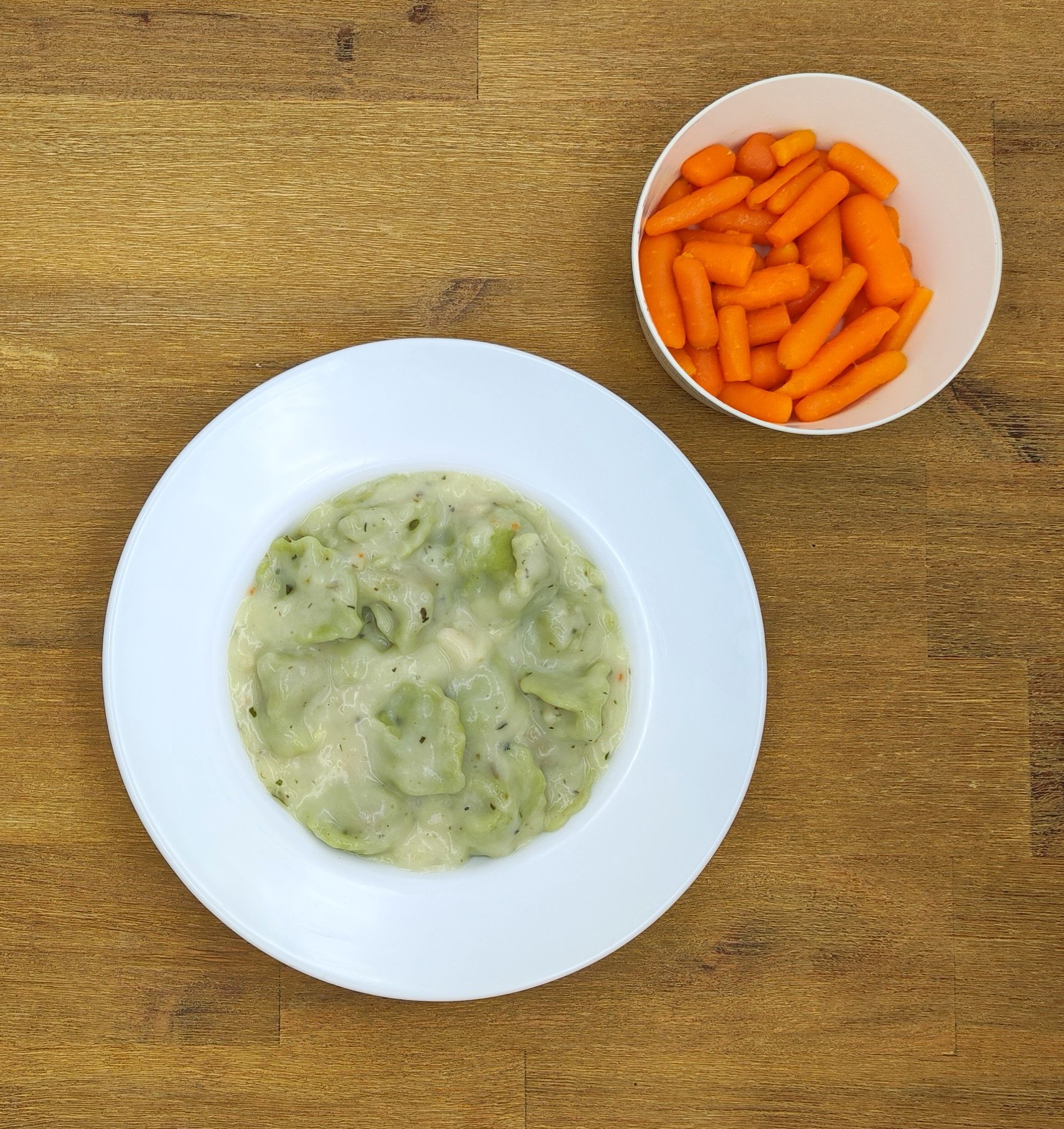Weiße Schüssel mit grüner Suppe, Schüssel mit orangefarbenen Karotten auf einem Holztisch.