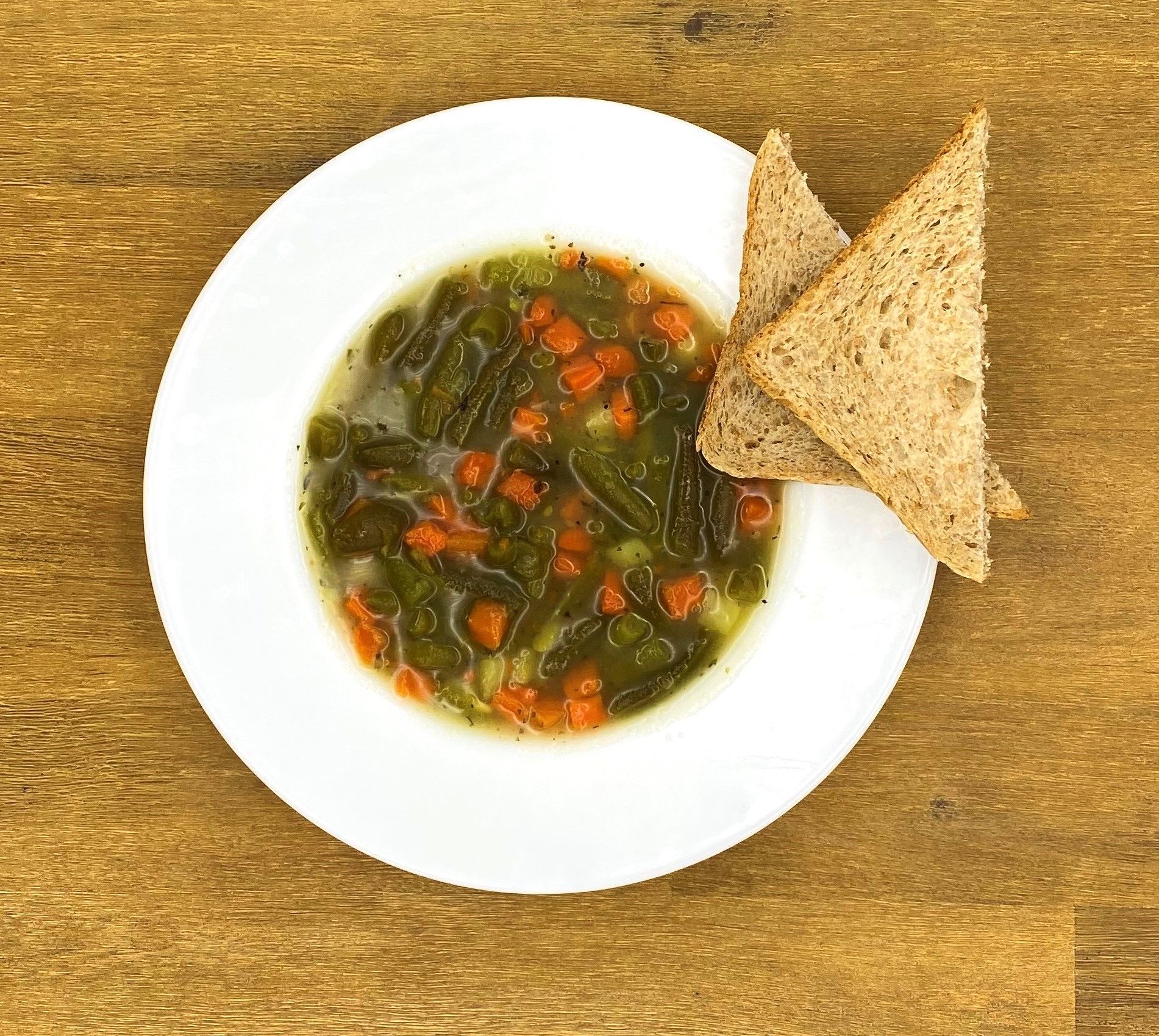 Eine Schüssel grüne Suppe mit orangefarbenen Karotten und zwei Scheiben Toast auf einem Holztisch.
