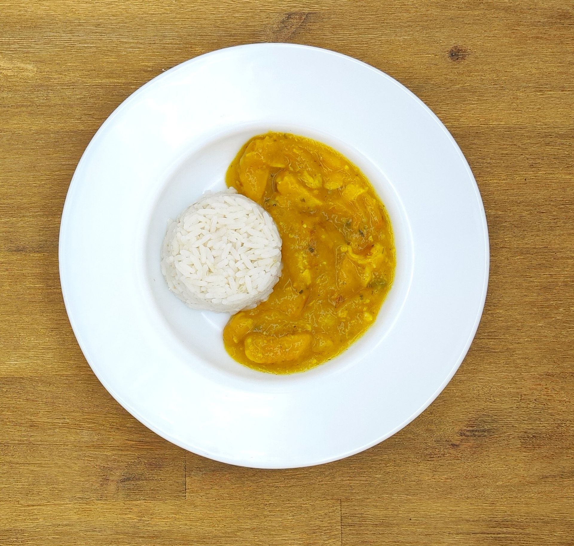Weißer Teller mit Reis und gelbem Curry auf einem Holztisch.
