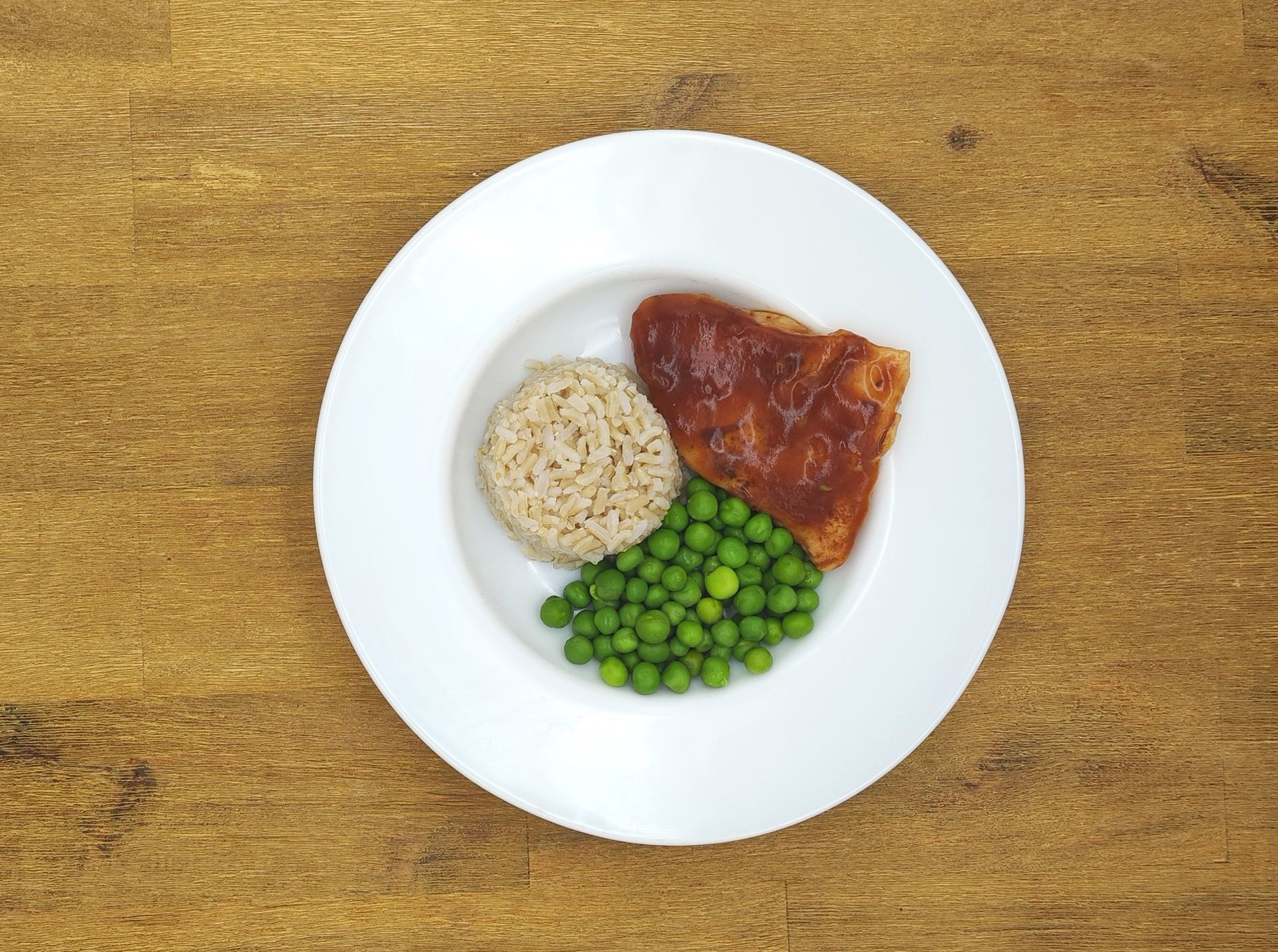 Teller mit Lachs, Erbsen und Reis. Der Lachs ist mit einer roten Soße überzogen.