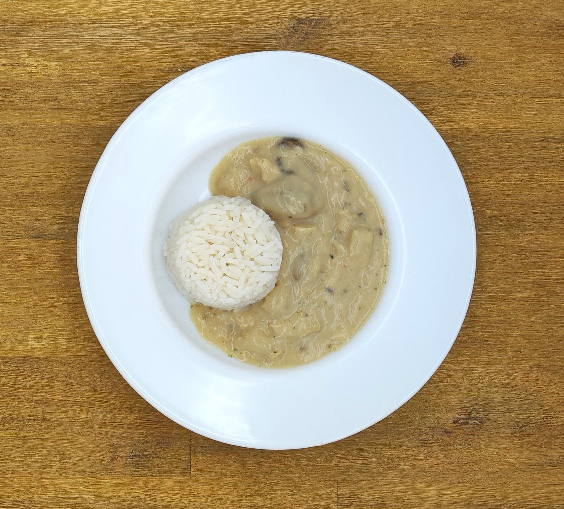 Weißer Teller mit Reis und cremiger Pilzsoße auf einem Holztisch.