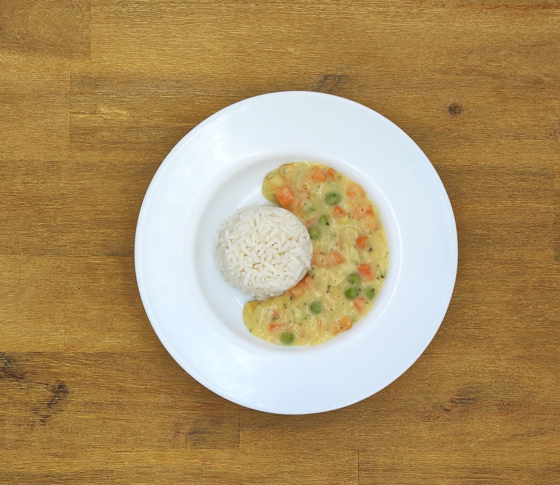 Weißer Teller mit Reis und Gemüsesauce auf einem Holztisch.