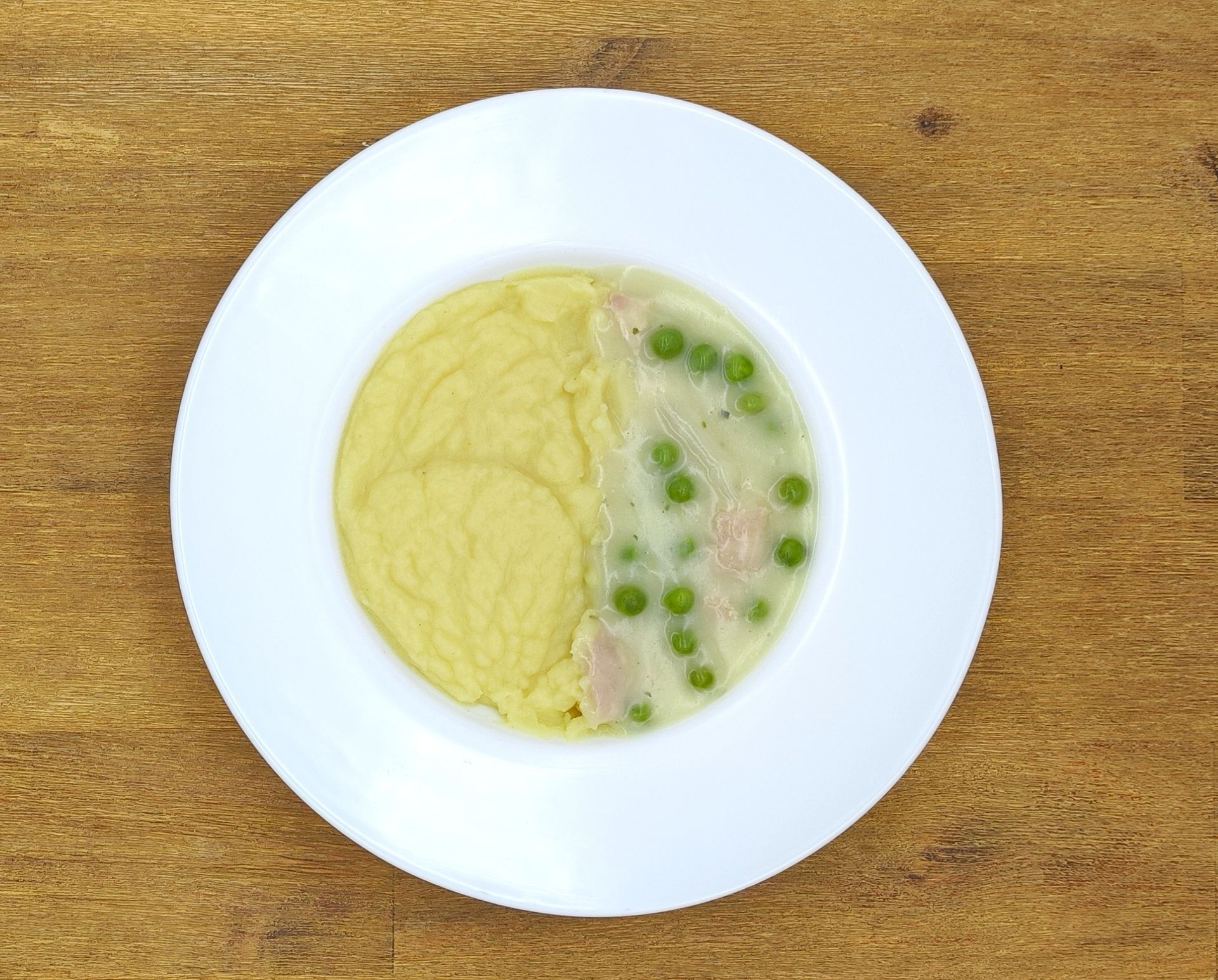 Weißer Teller mit Kartoffelpüree links und Hühnchen mit Erbsen in Soße rechts.