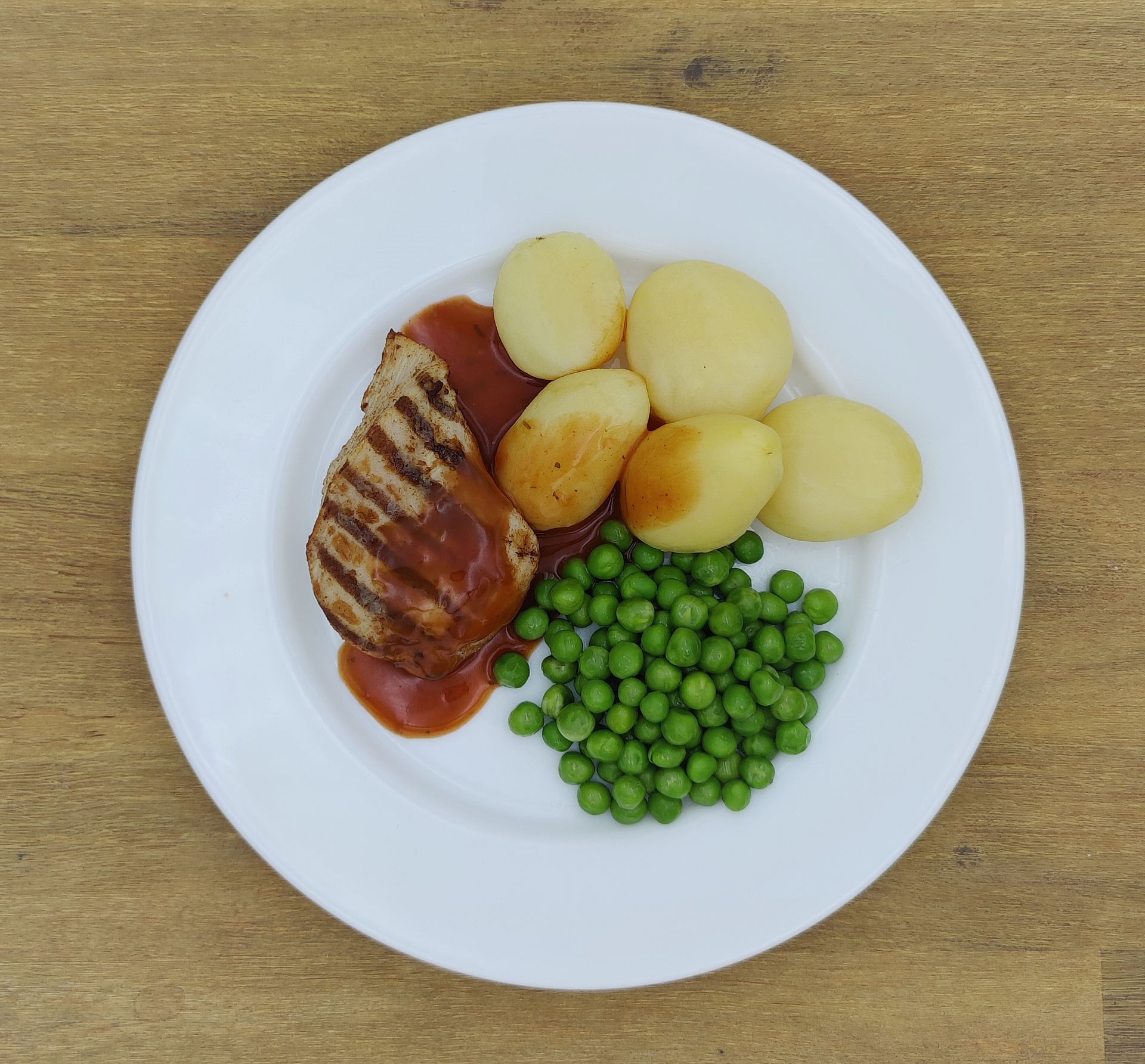Teller mit Essen: Gegrilltes Fleisch mit Soße, Kartoffeln und Erbsen.