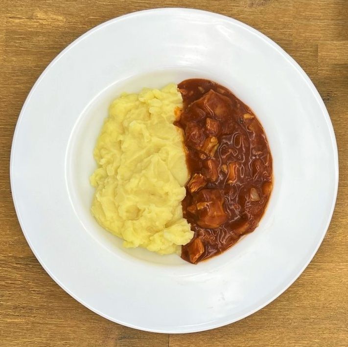 Ein Teller mit Kartoffelpüree und Eintopf in einer weißen Schüssel auf einer Holzoberfläche.