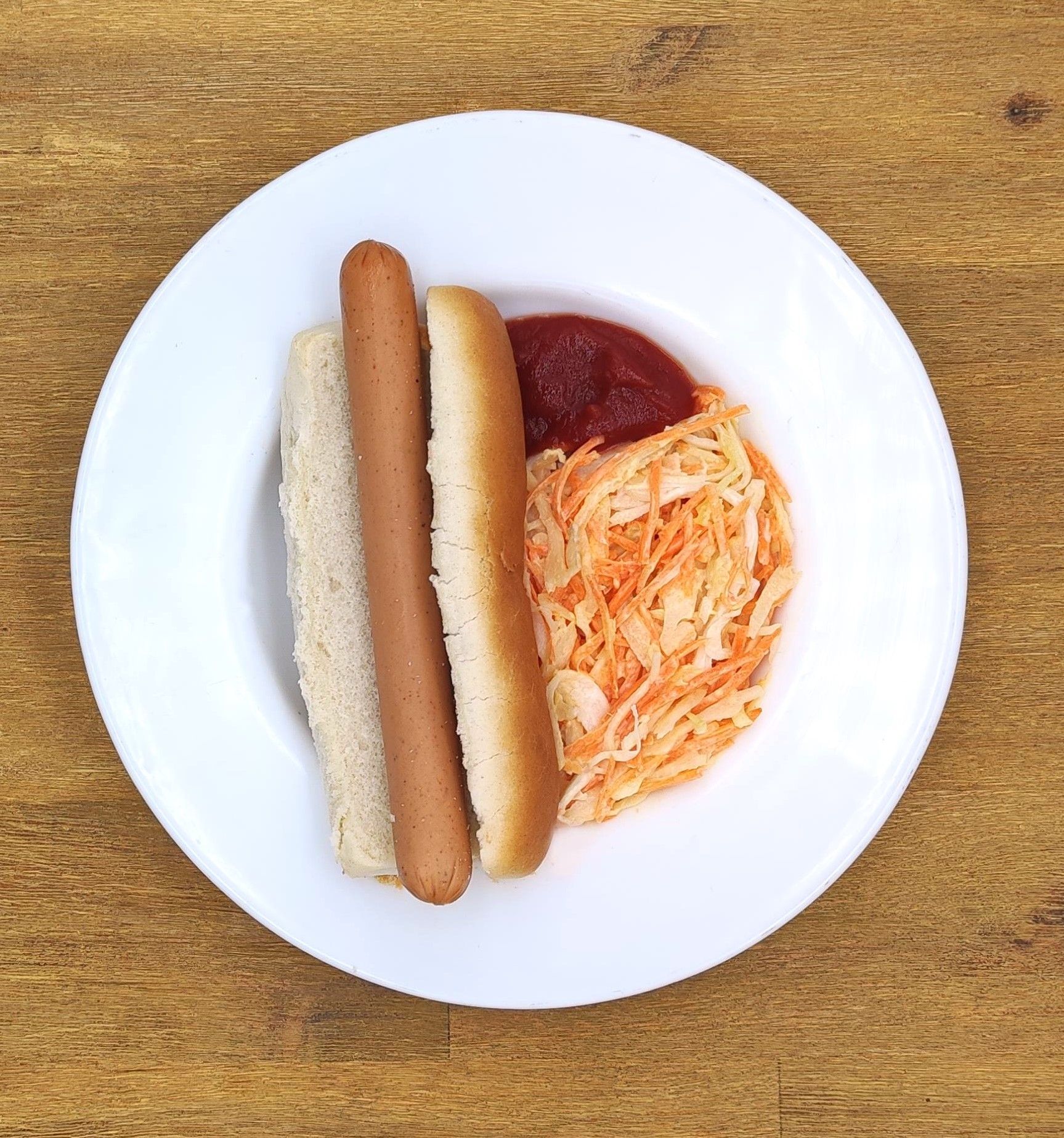 Hotdog im Brötchen mit Krautsalat und Ketchup auf einem weißen Teller.