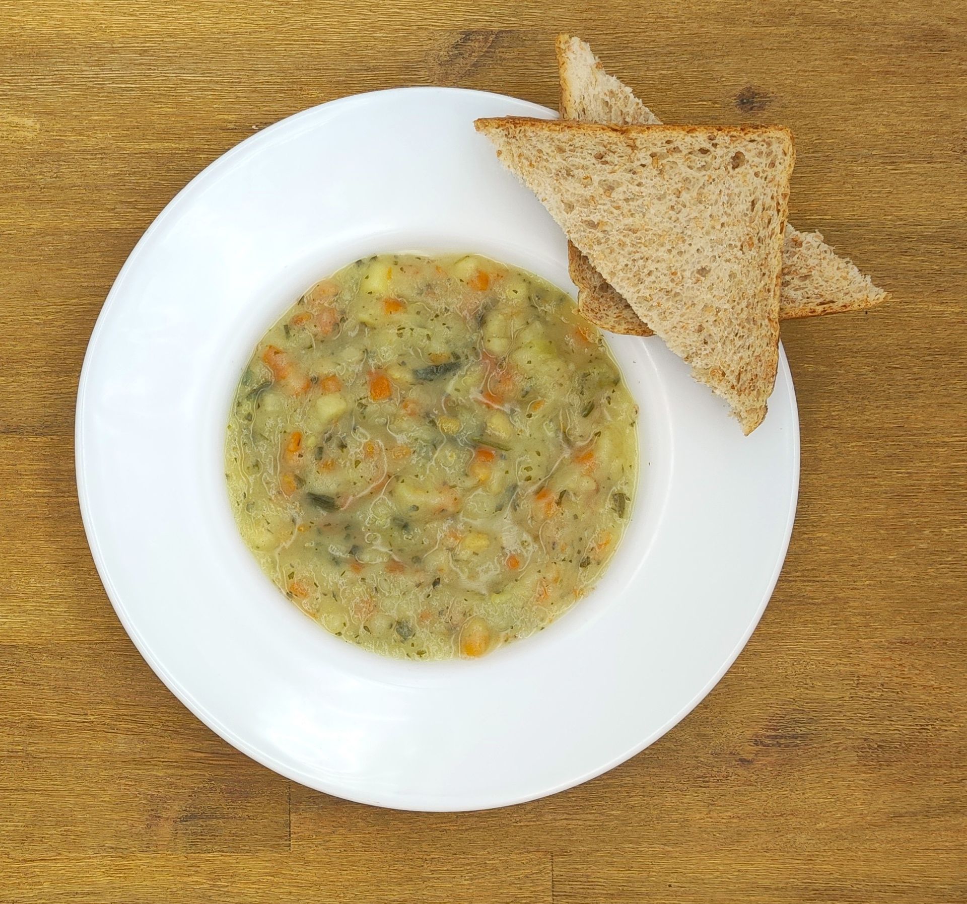 Suppe in einer weißen Schüssel mit zwei Scheiben Toast auf einer Holzplatte.