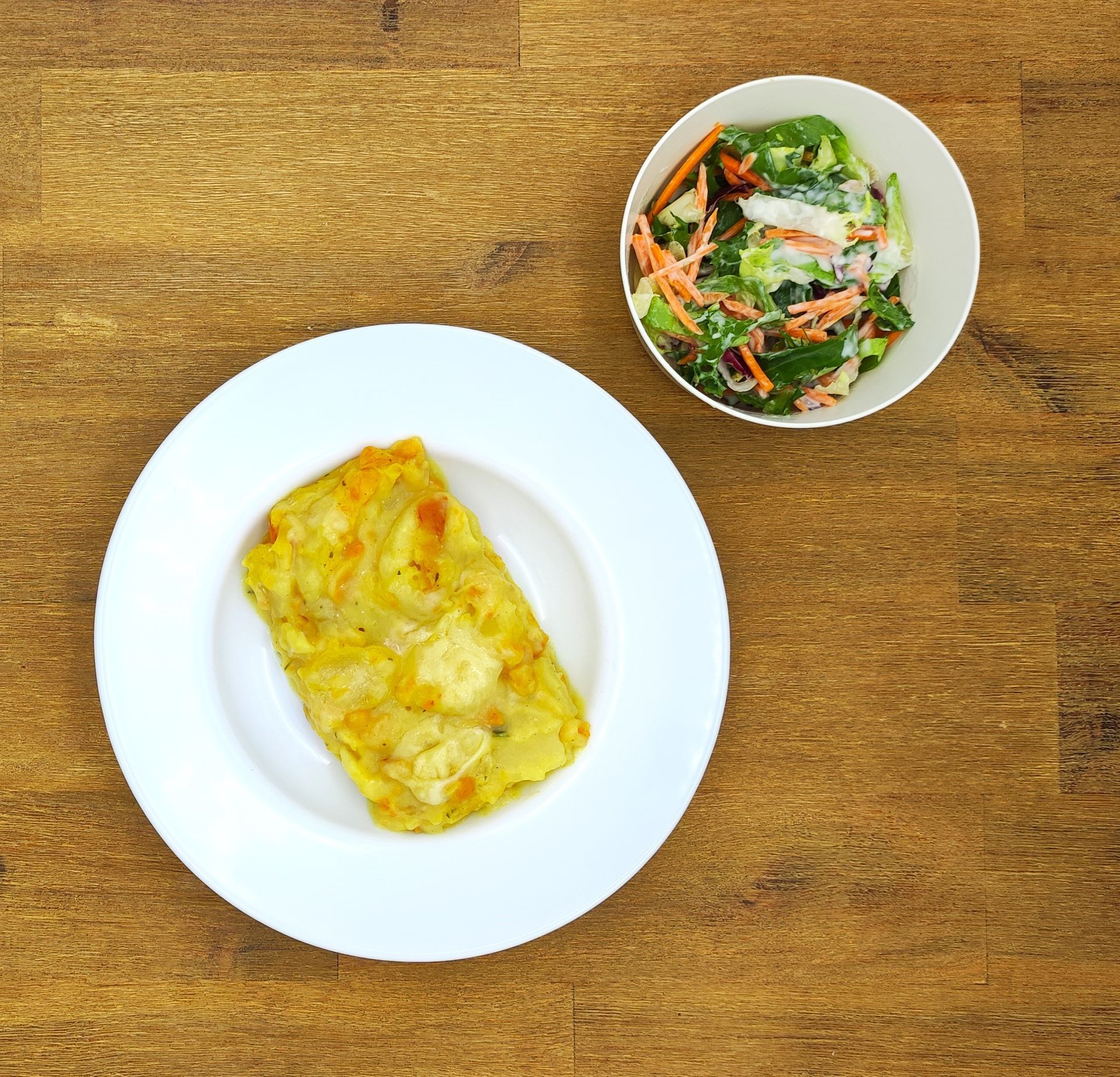 Ein Teller mit Essen und ein Beilagensalat auf einem Holztisch.