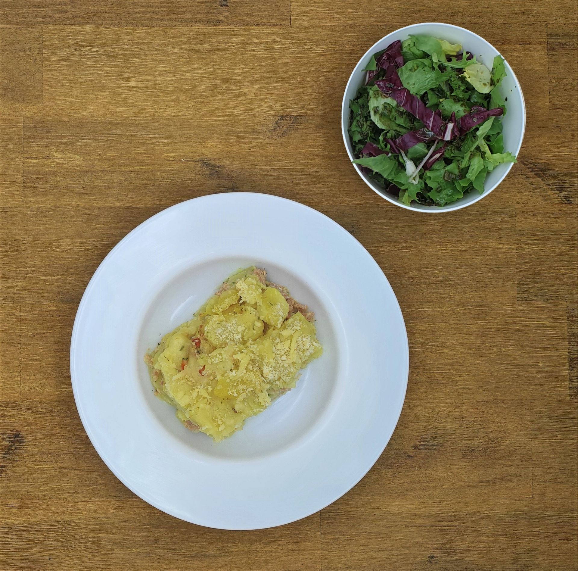 Teller mit gelbem Auflauf und kleiner Schüssel Salat auf einem Holztisch.