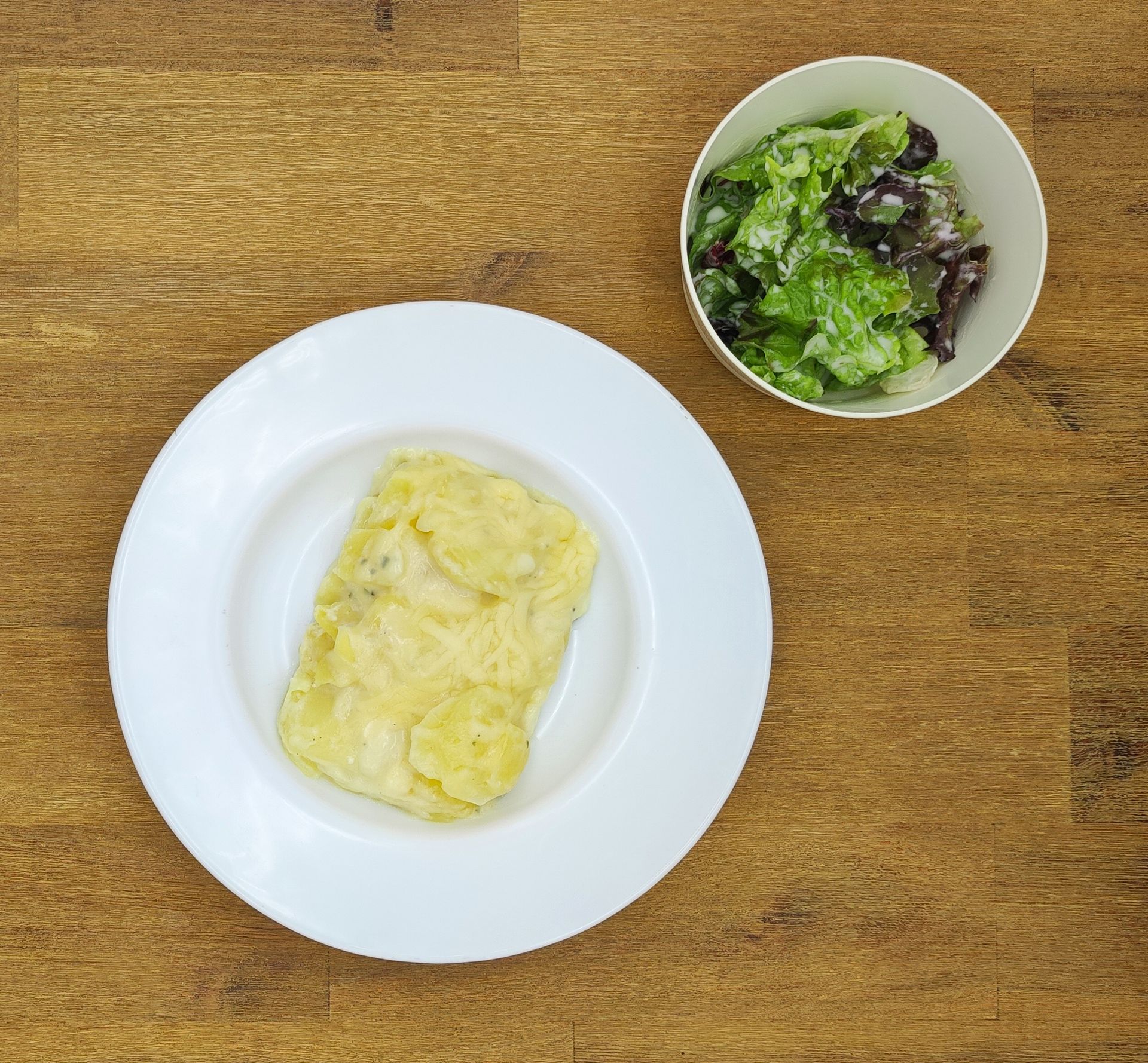 Weißer Teller mit gefaltetem Ei, Schüssel mit Salat auf einem Holztisch.