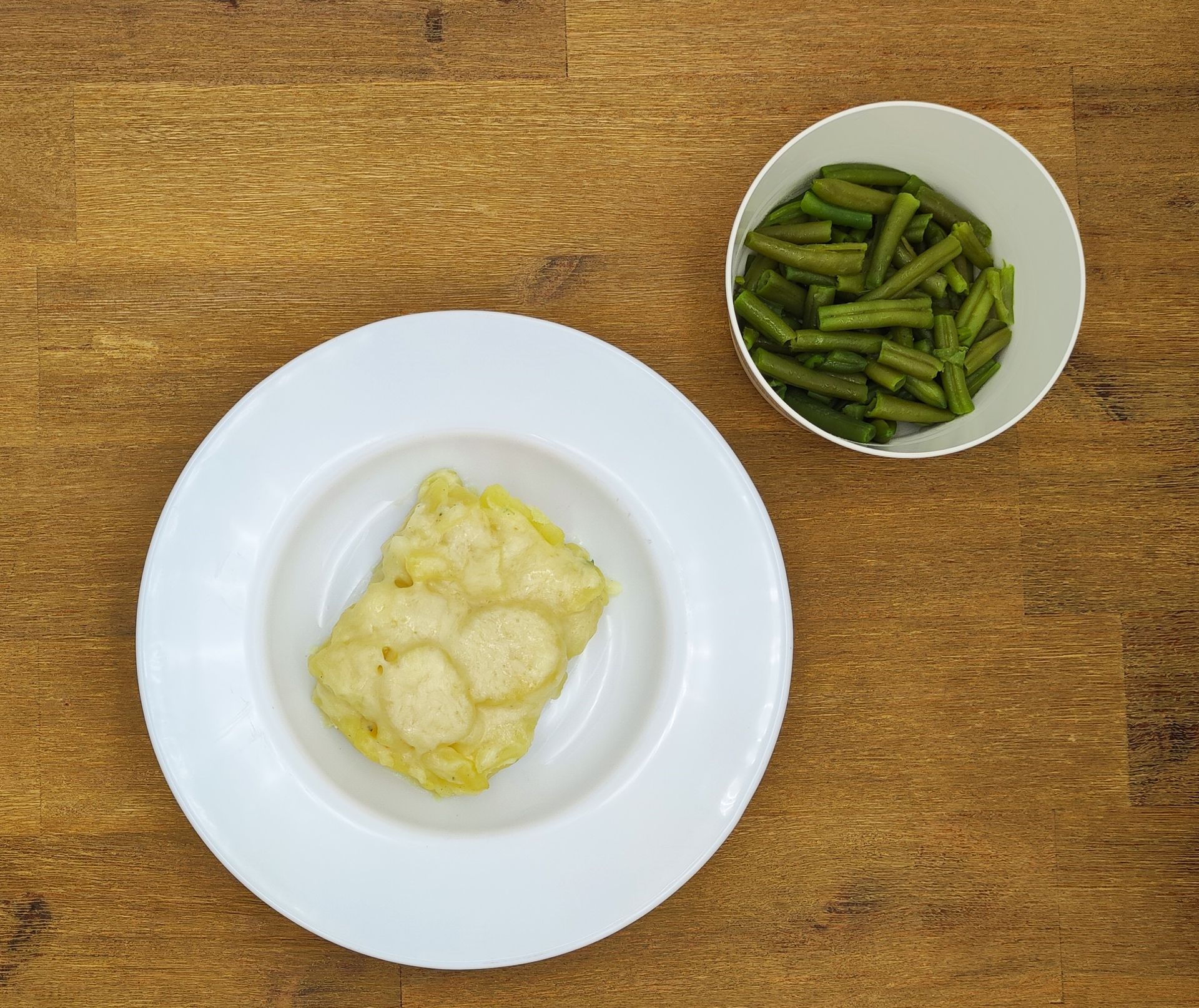 Teller mit frittiertem Essen und Schüssel mit grünen Bohnen auf einer Holzoberfläche.