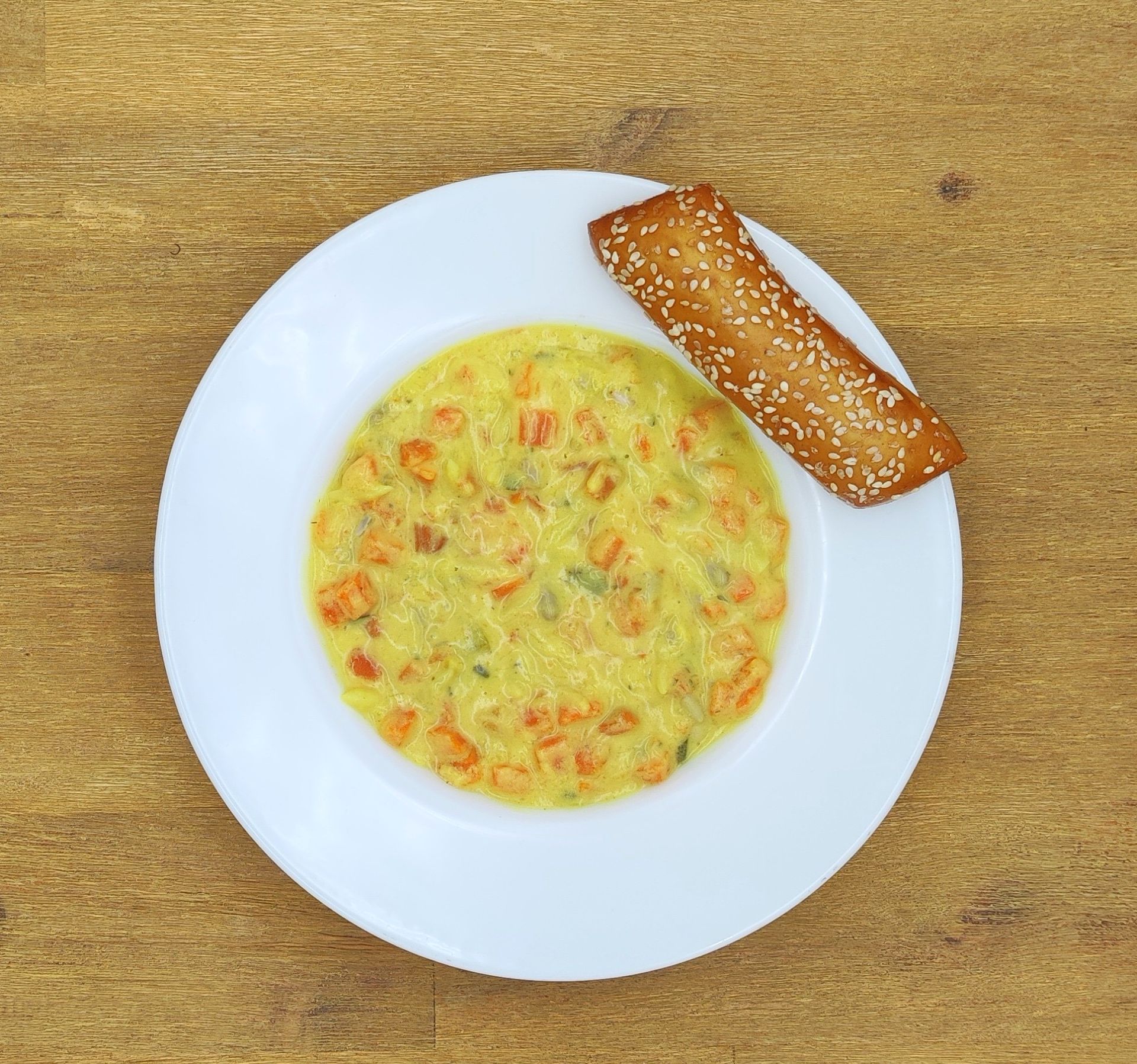 Ein Teller mit cremefarbenem, gelbem Essen mit Orangenstückchen und einem Sesam-Grissini auf einem Holztisch.