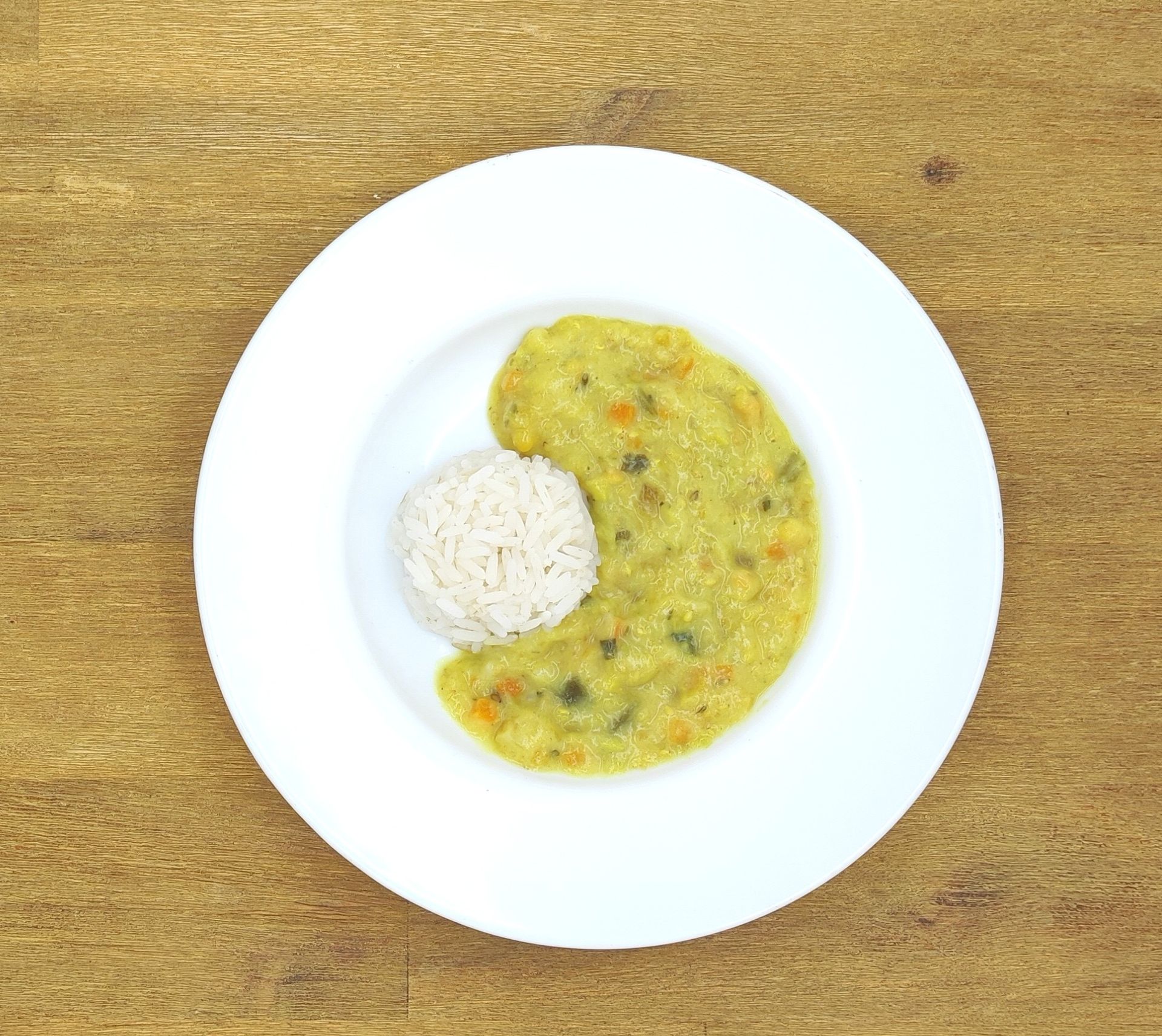 Weiße Schüssel mit Linsensuppe und Brot auf einer Holzoberfläche.