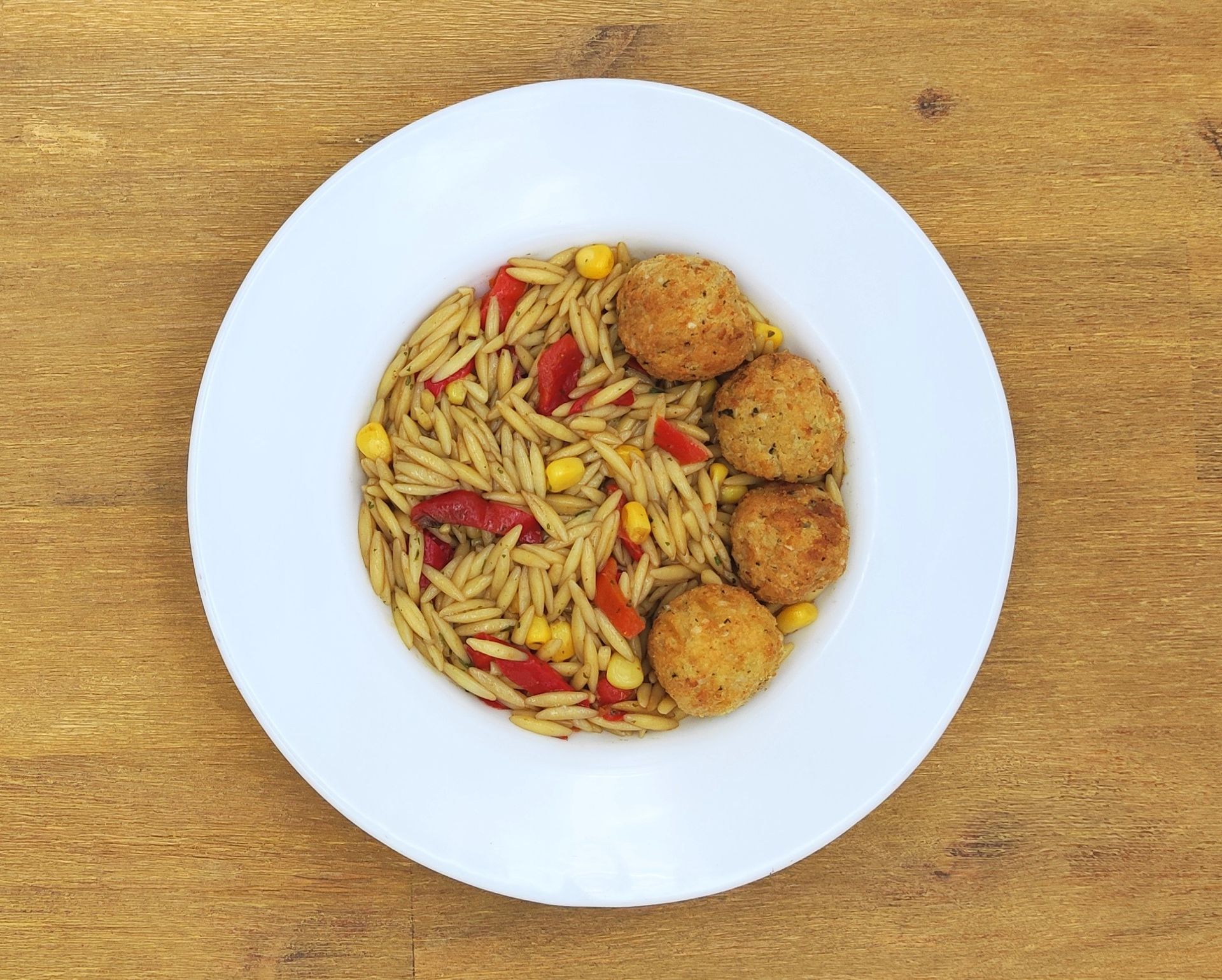 Weißer Teller mit Orzo-Nudeln, roter Paprika, Mais und vier goldbraunen Fleischbällchen.