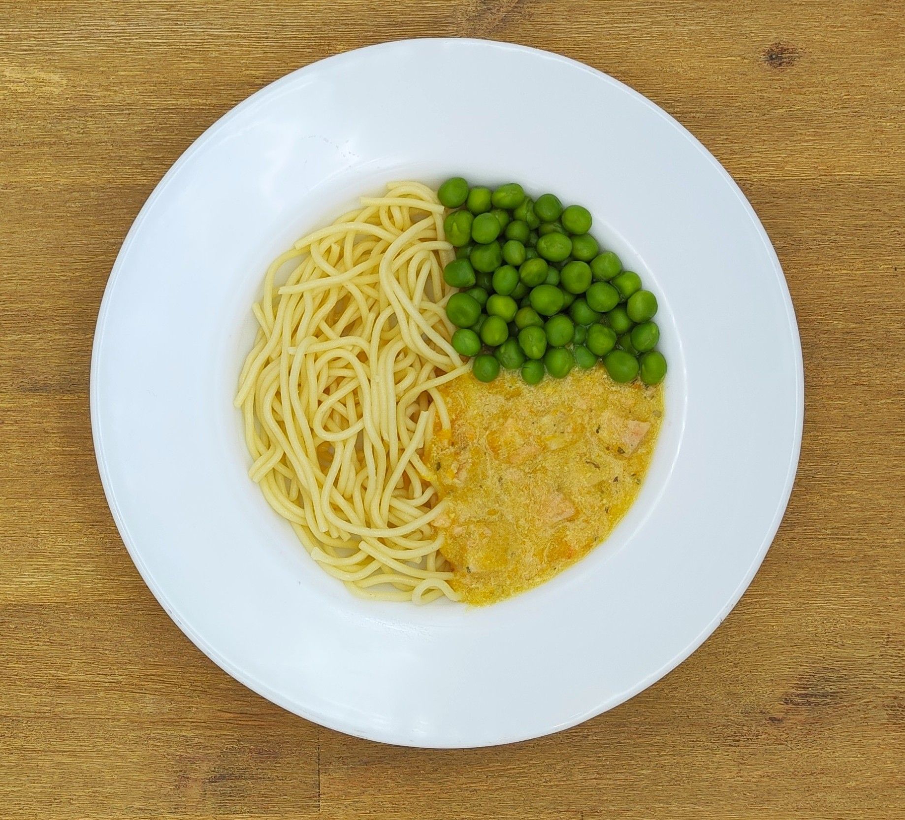Ein Teller mit Spaghetti, Erbsen und cremiger Soße auf einem Holztisch.