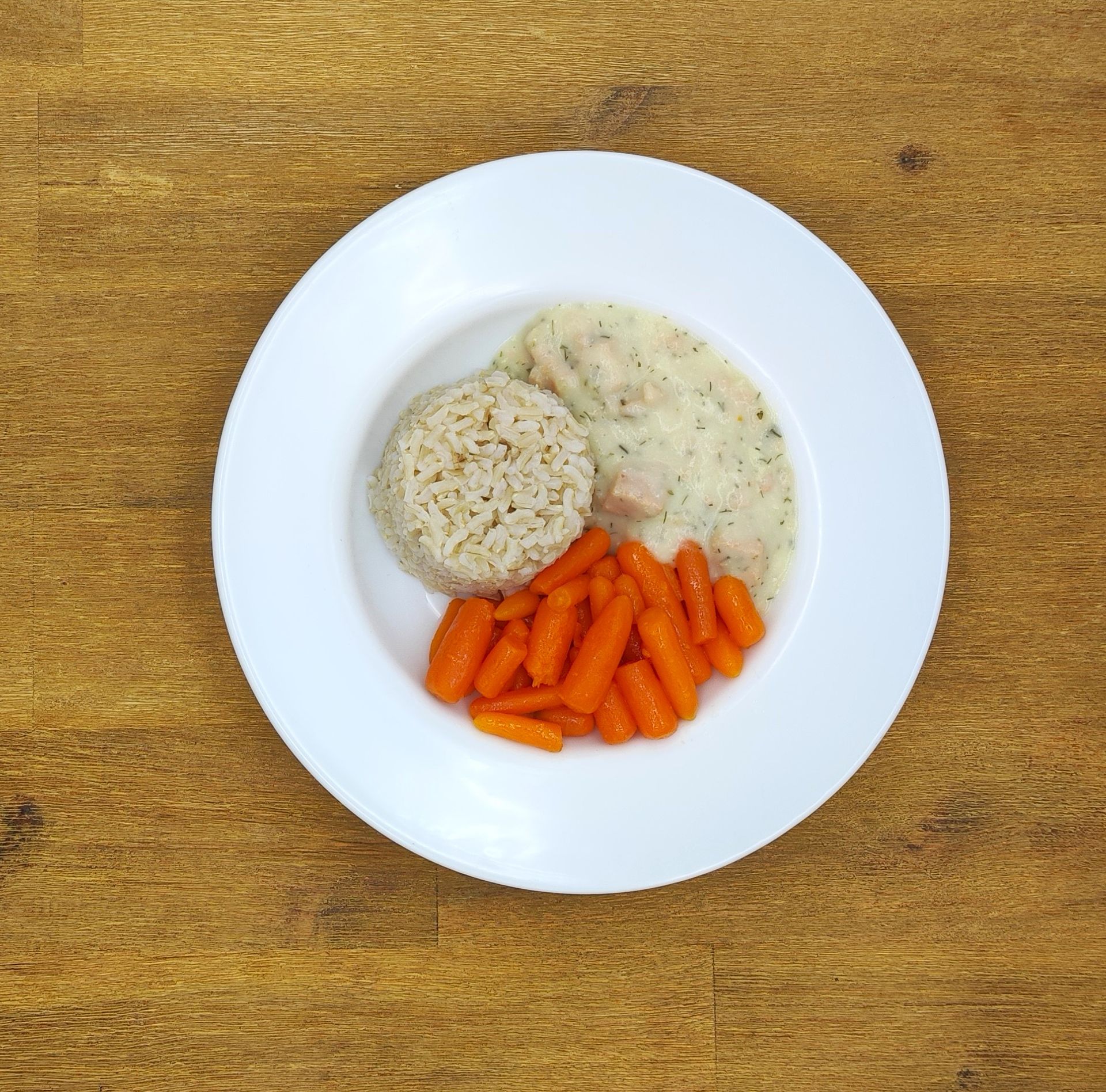 Ein Teller mit Essen: Reis, Karotten und Hühnchen in Sahnesauce auf einem Holztisch.