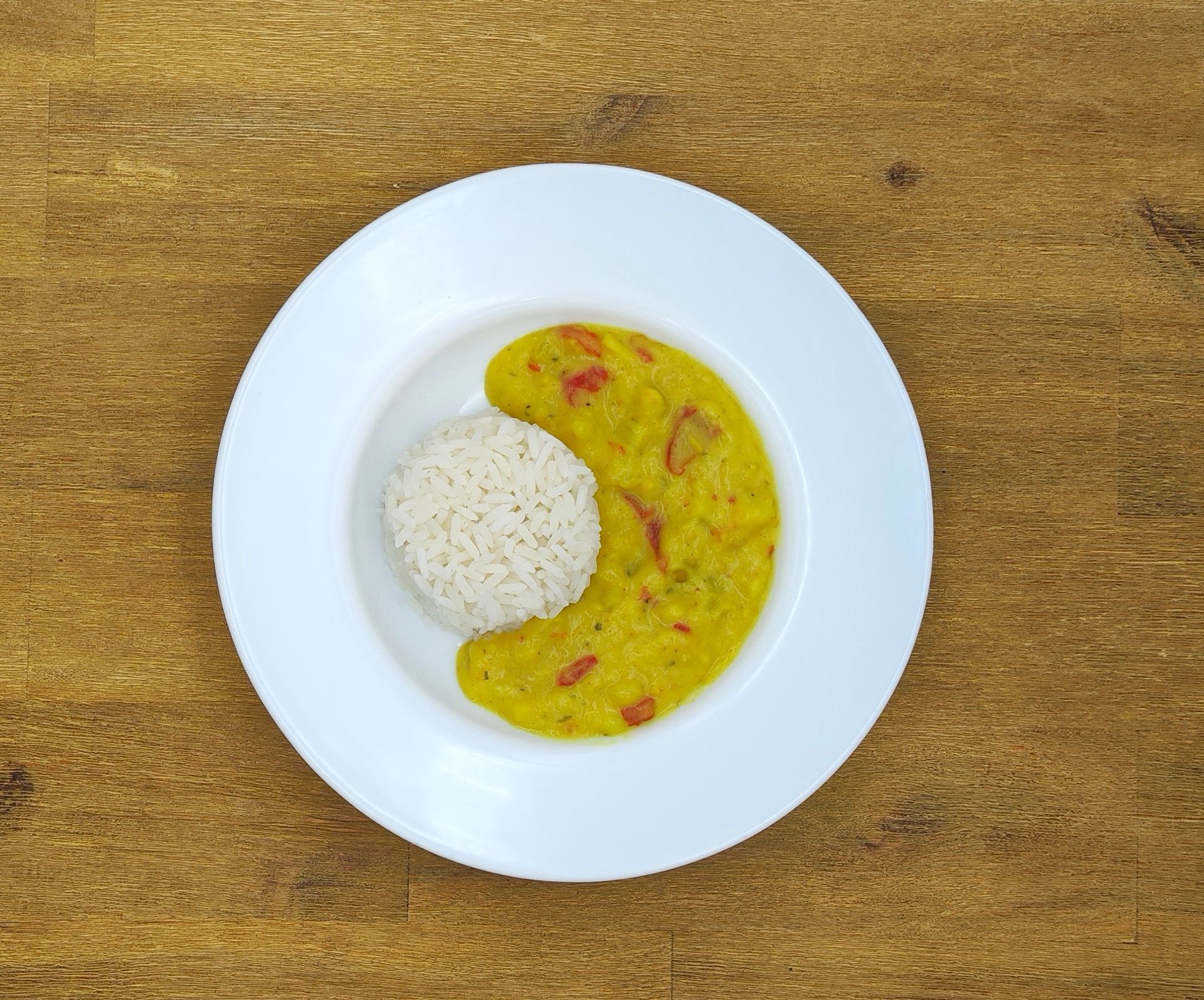 Ein weißer Teller mit gelbem Curry und einer Kugel weißem Reis auf einem Holztisch.