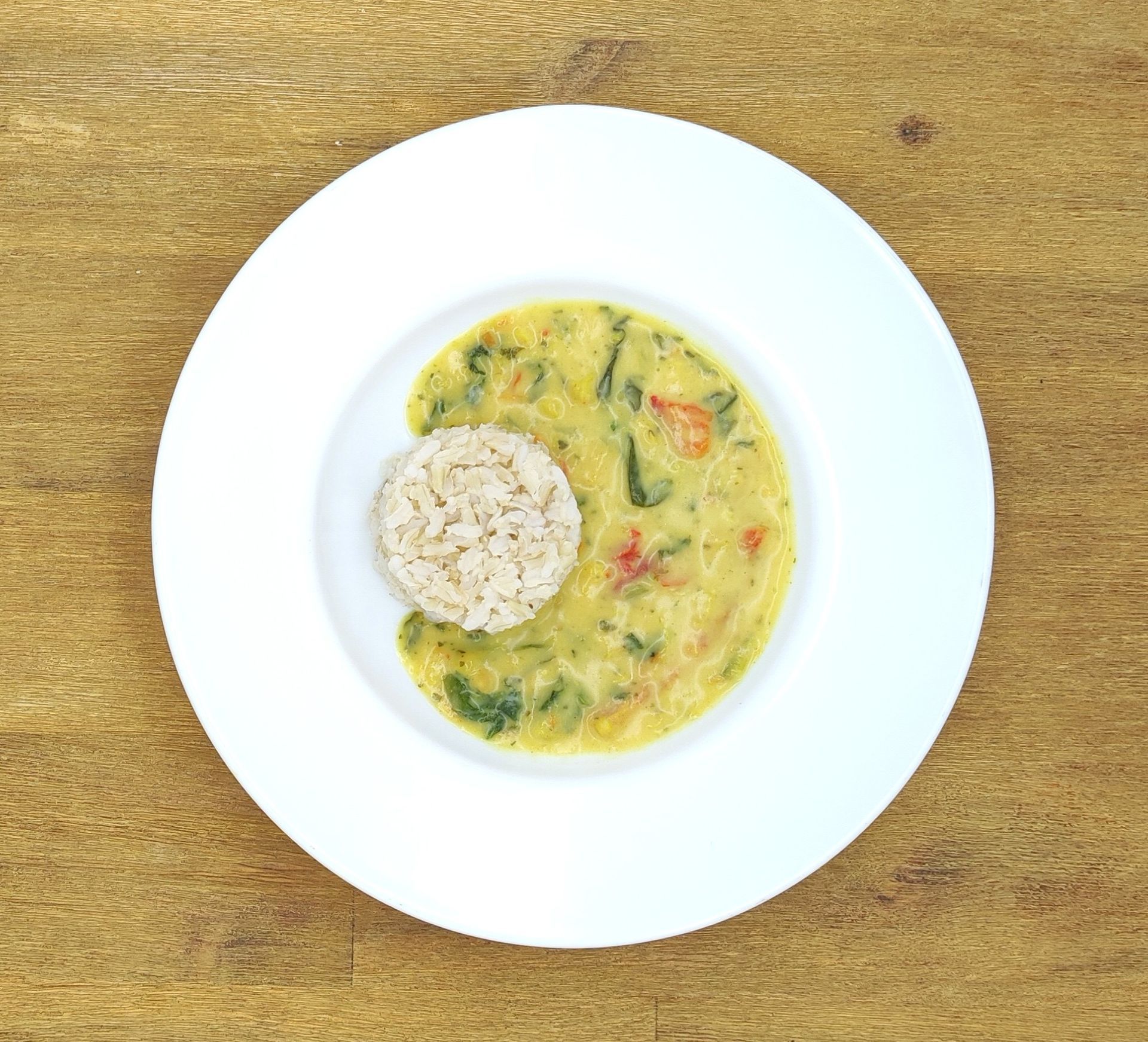 Weißer Teller mit Reis und Curry auf einer Holzoberfläche.