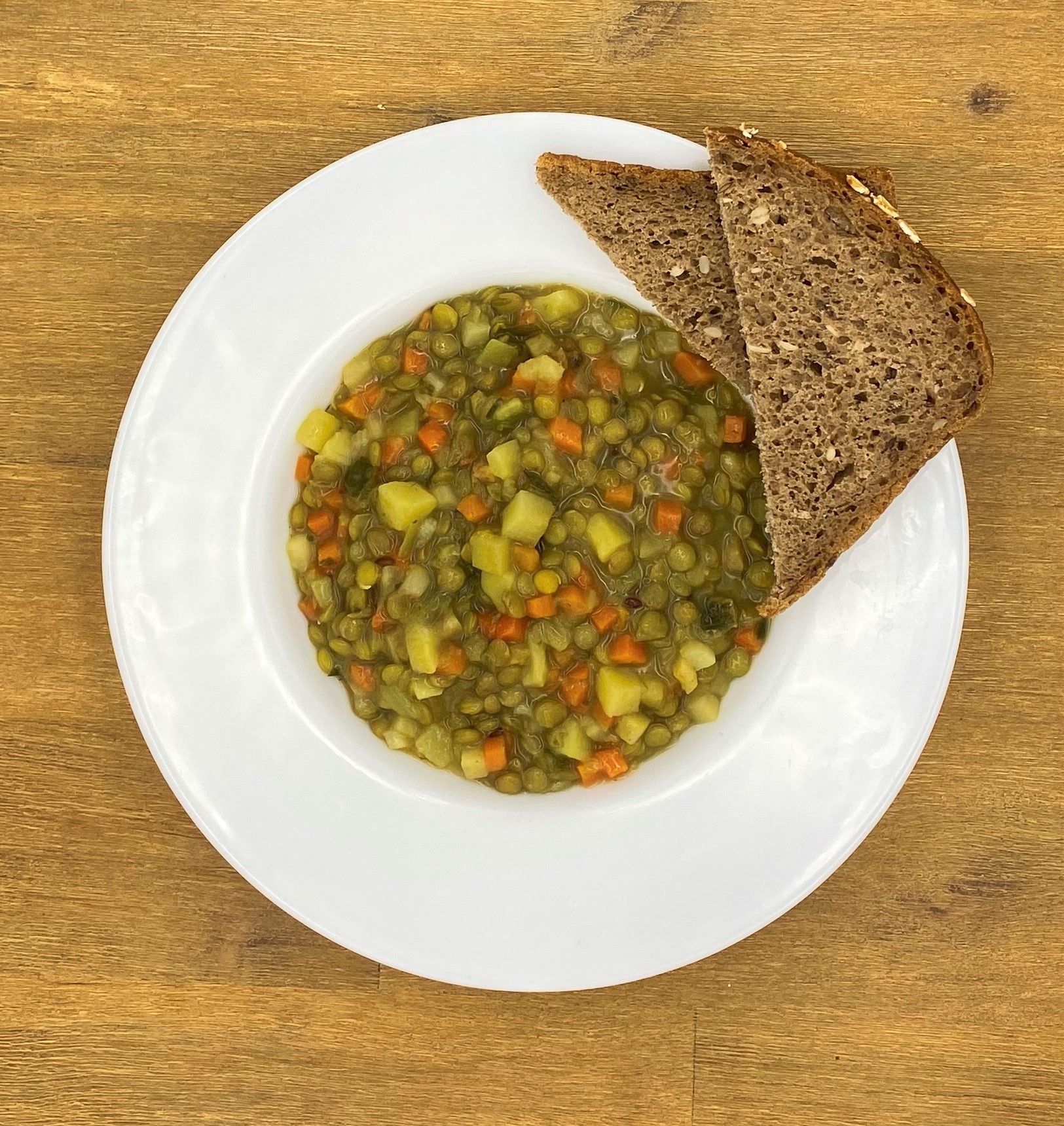 Linsensuppe mit Karotten und Kartoffeln, serviert mit zwei Scheiben dunklem Brot auf einem weißen Teller.