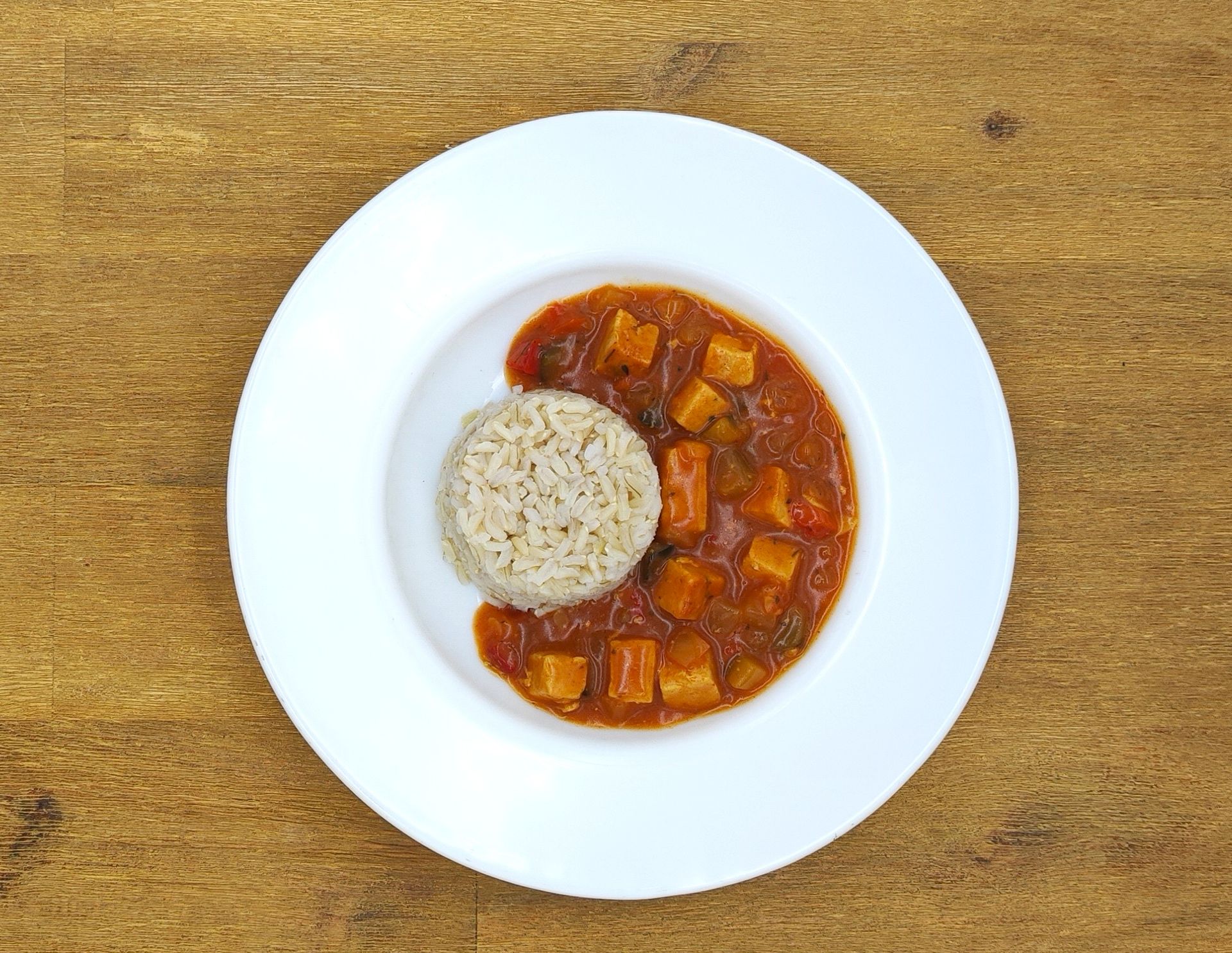 Weißer Teller mit braunem Reis und gewürfeltem Eintopf in Tomatensoße.
